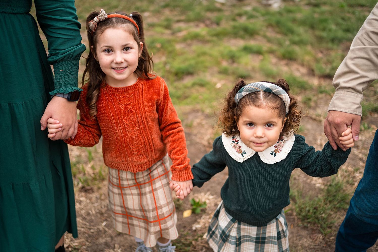 two sisters hold each other's hands and their parents and smile at the camera during their family session in Lee's Summit
