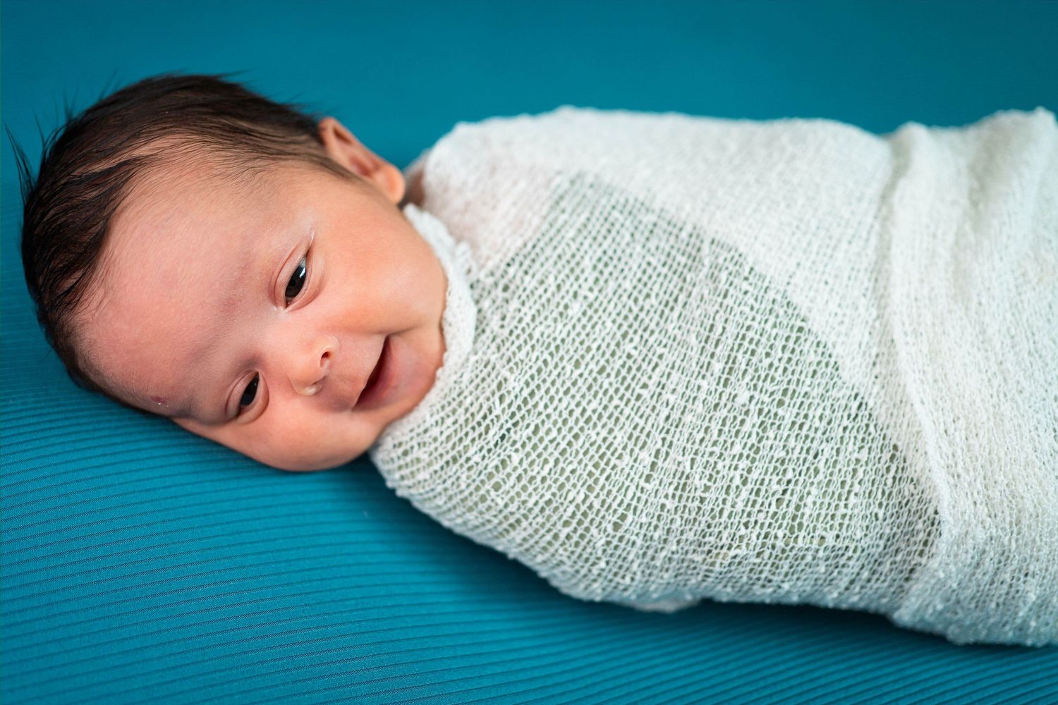 A baby smiles at the camera while in a swaddle during his newborn session in Knob Noster, MO