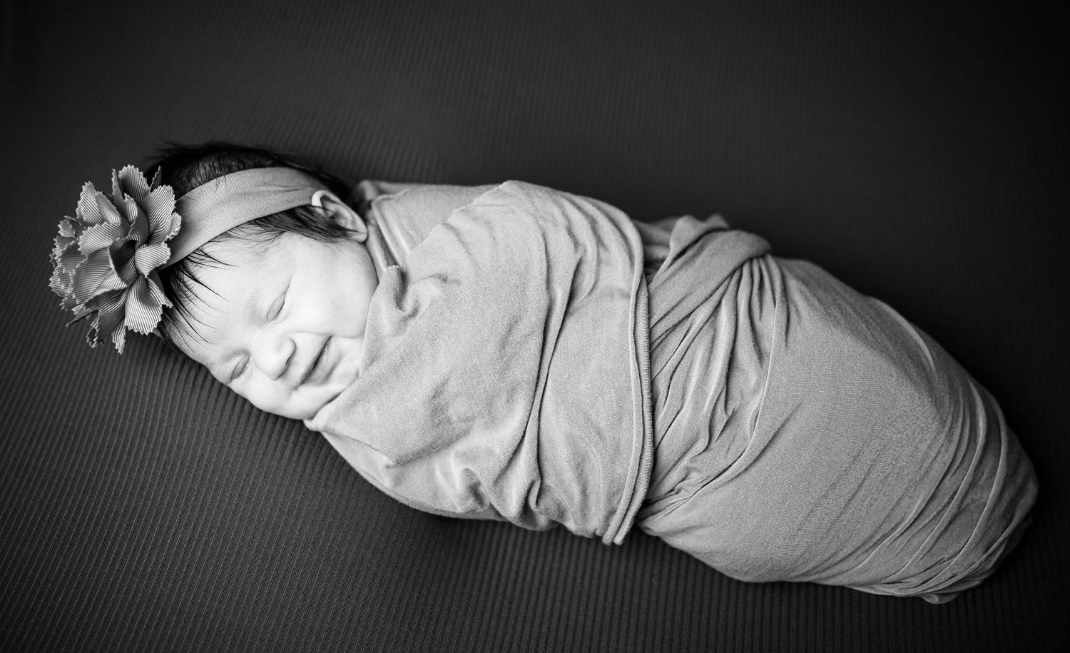 A baby is all snuggled in a wrap and headband and smiling during her newborn session in Warrensburg, MO