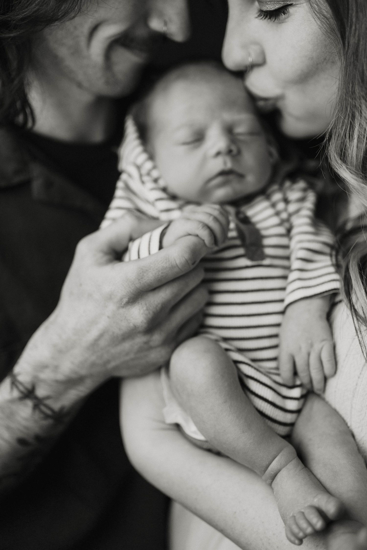 Mom and dad cuddle in to baby and give a kiss on the head during their in-home newborn photography session in Lee's Summit