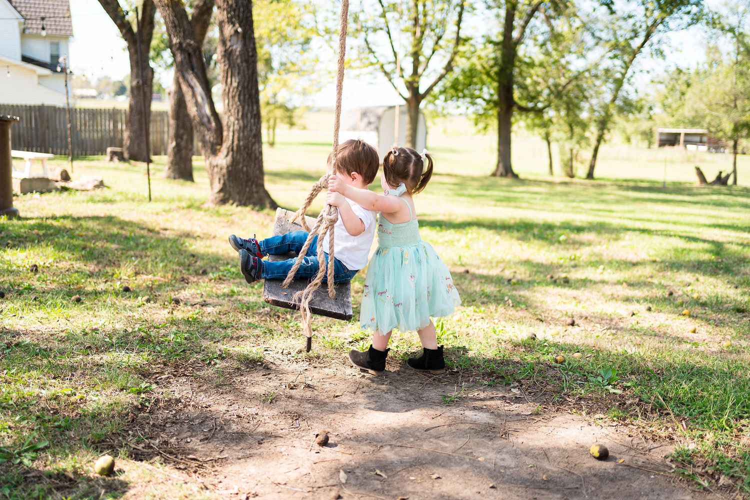 A sister pushes her brother on a swing during their family photo session in Warrensburg