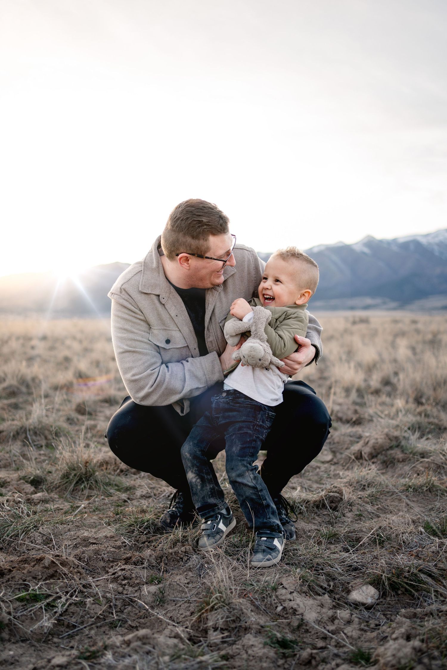 A parent and child share a tender moment in a field with mountains in the background.