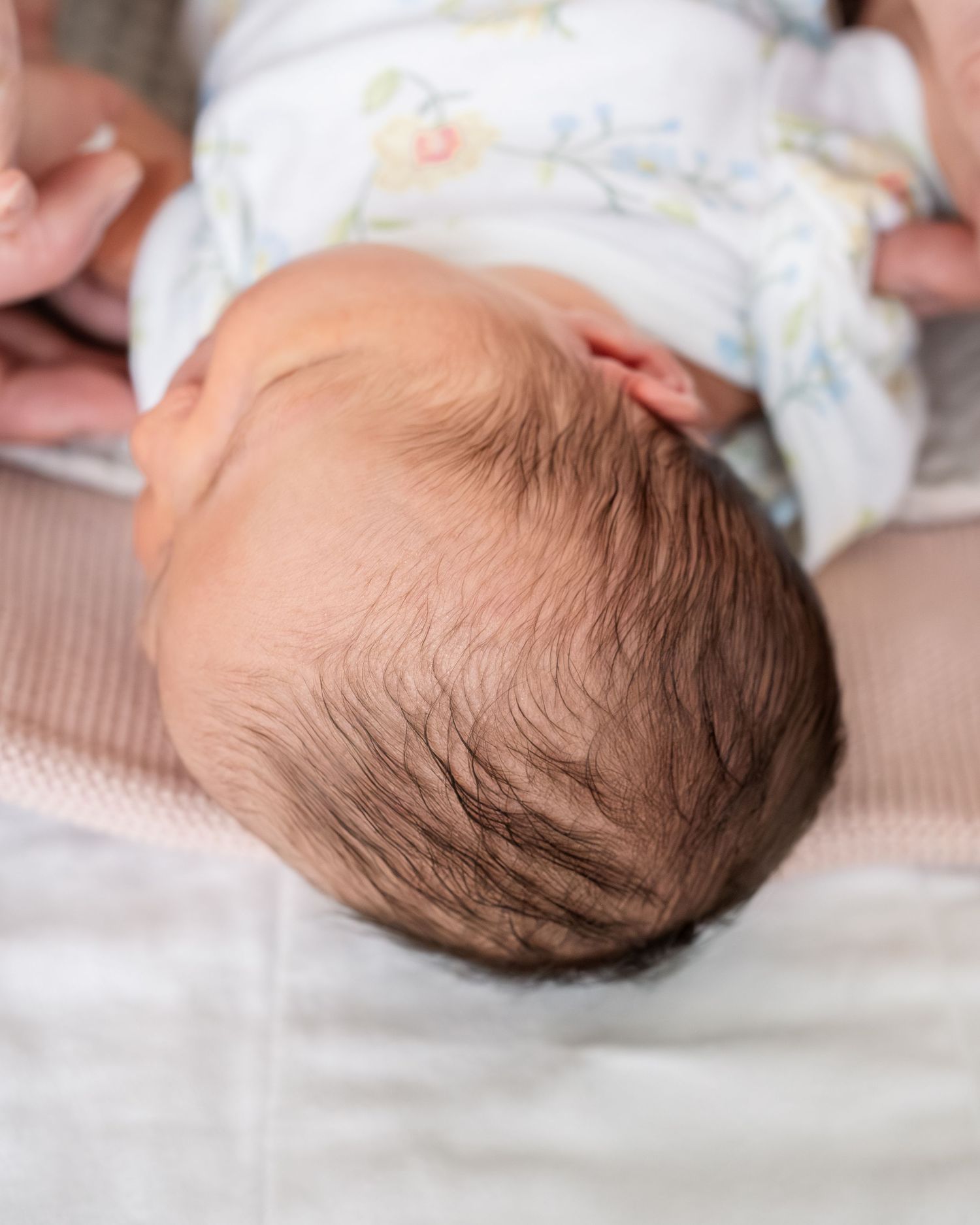Close-up top view of a newborn baby's head with fine dark hair, resting on a soft white blanket.