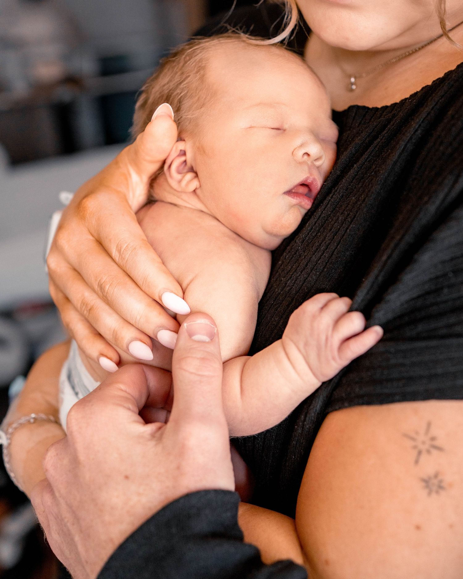Sleeping newborn baby cradled in mothers arms wearing black top with star tattoo on wrist.