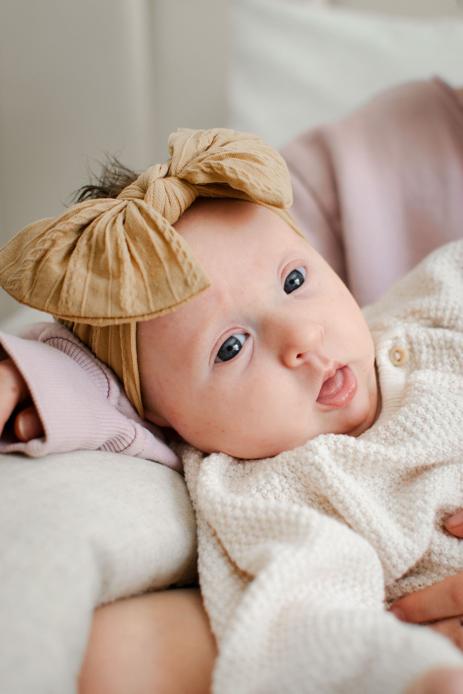 Infant wearing white knit clothing lying on soft blanket looking at camera with bright blue eyes.