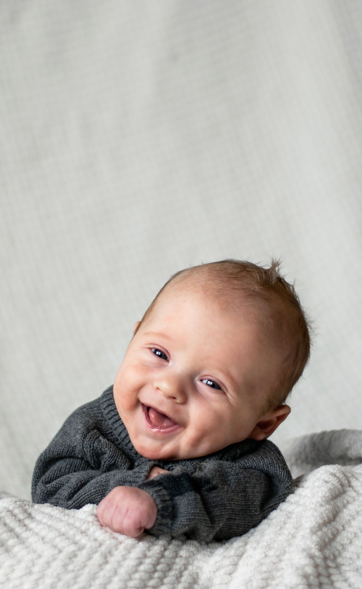 Happy baby in dark sweater lying on white knitted blanket.