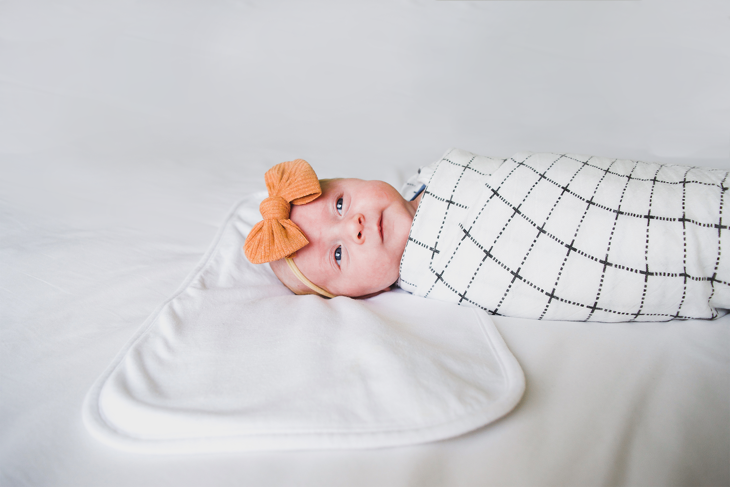Newborn baby sleeping peacefully wrapped in white and black patterned blanket.