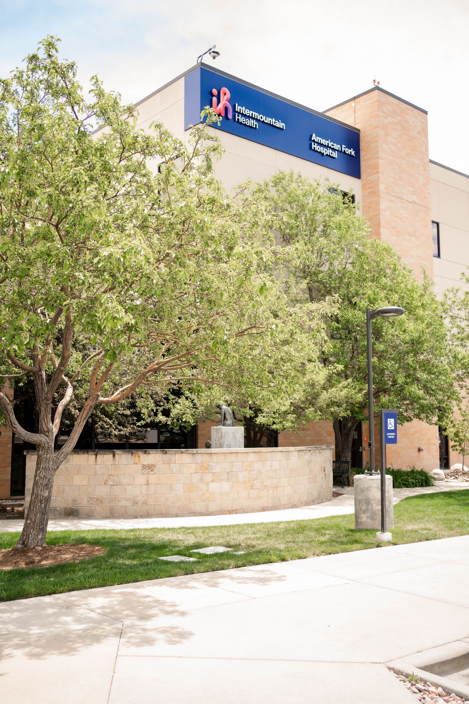 Intermountain Health American Fork Hospital exterior with modern architecture, trees, and walkway on a sunny day.