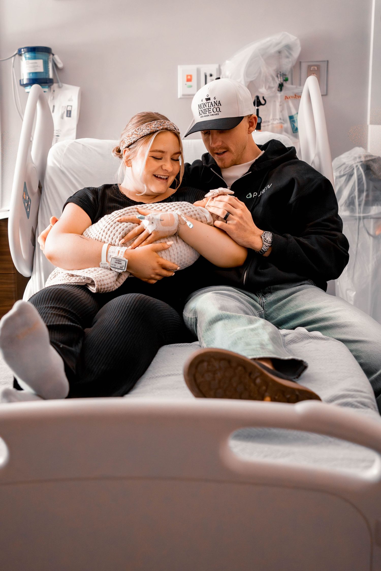 New parents joyfully holding their newborn baby together on a hospital bed, sharing a tender first family moment.