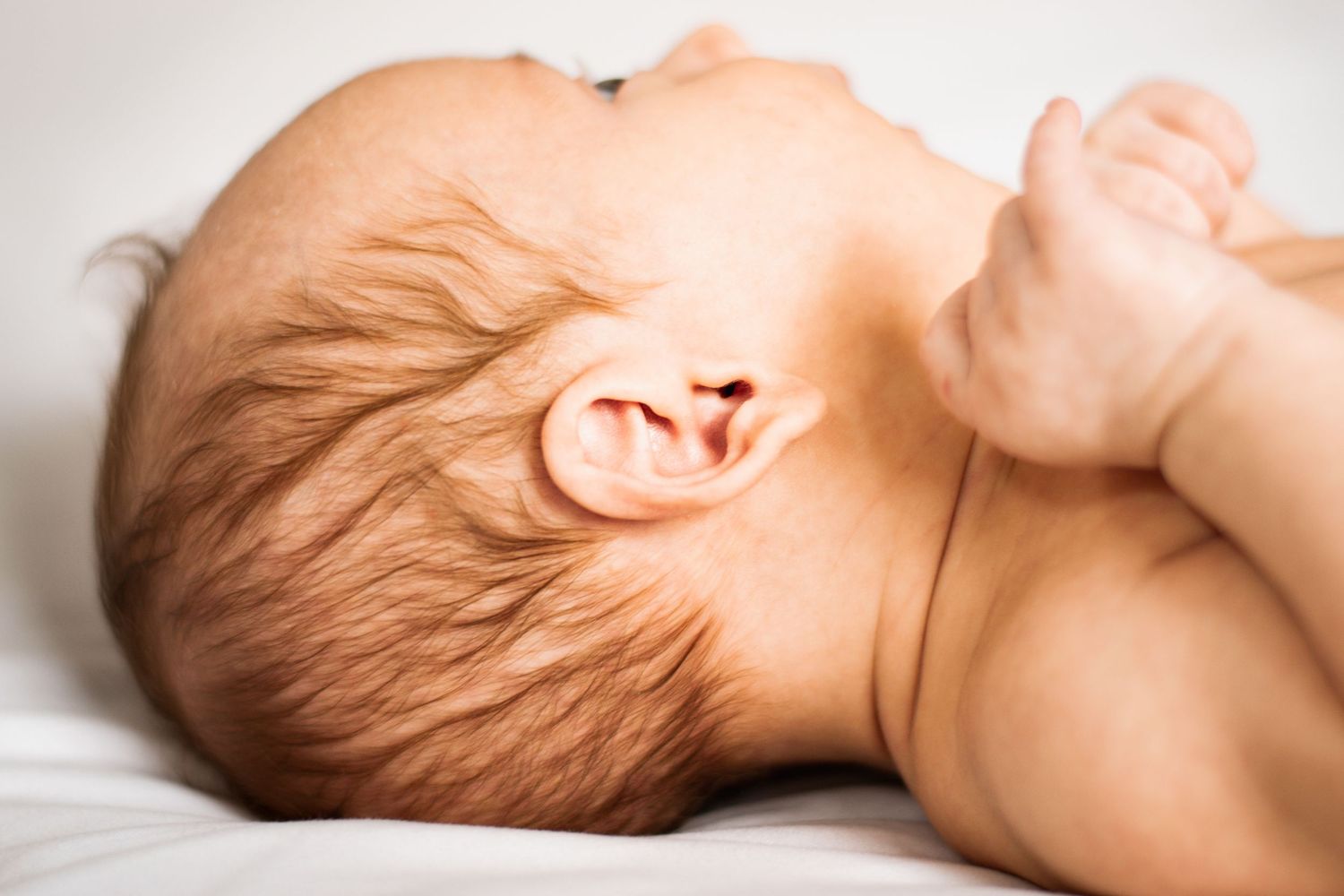 Newborn baby resting on white textured background.