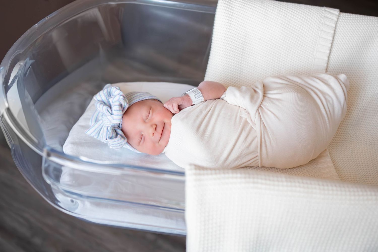 Newborn baby swaddled in white blanket sleeping peacefully in a modern bassinet.