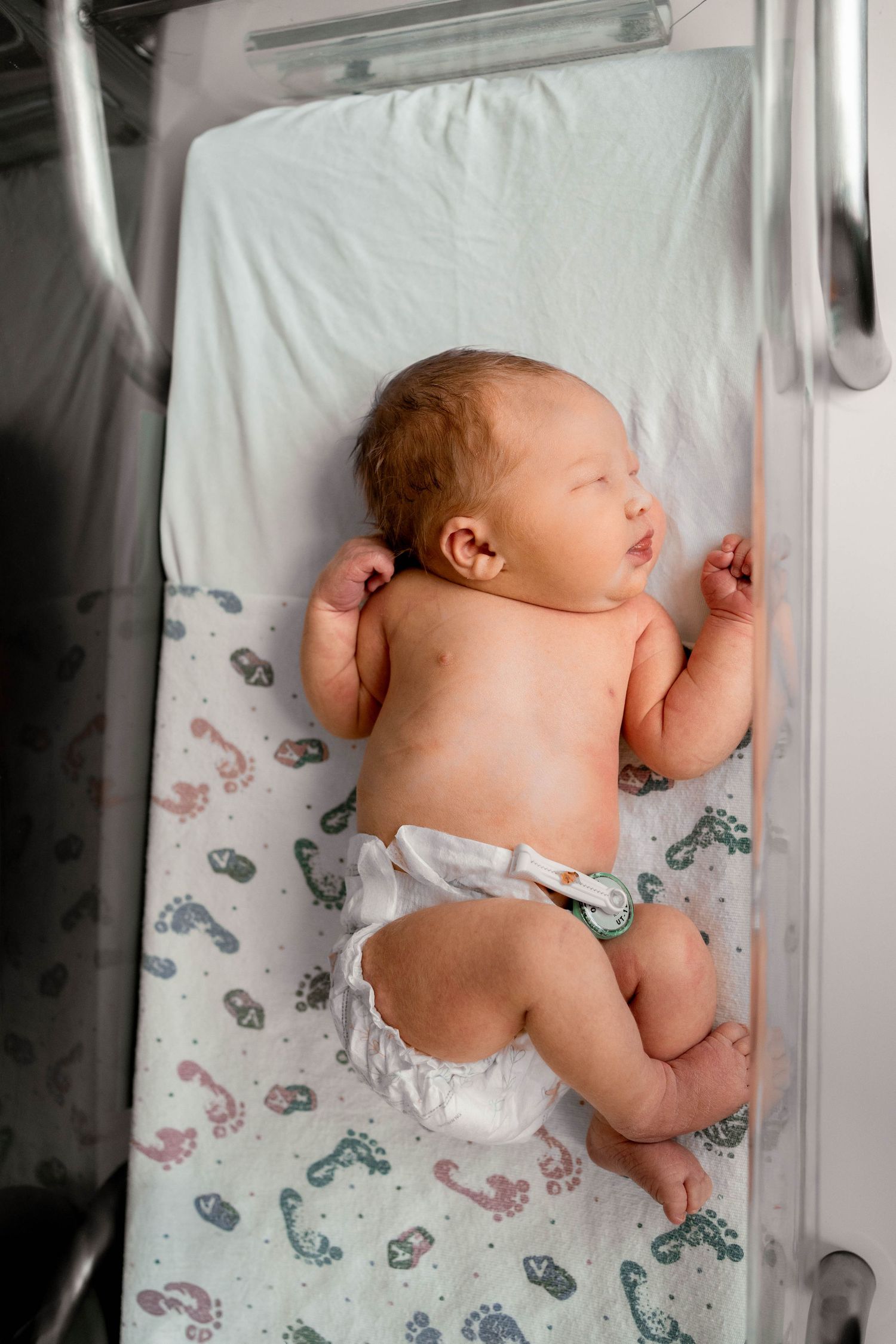 Newborn baby lying on back in hospital bassinet wearing only a diaper.