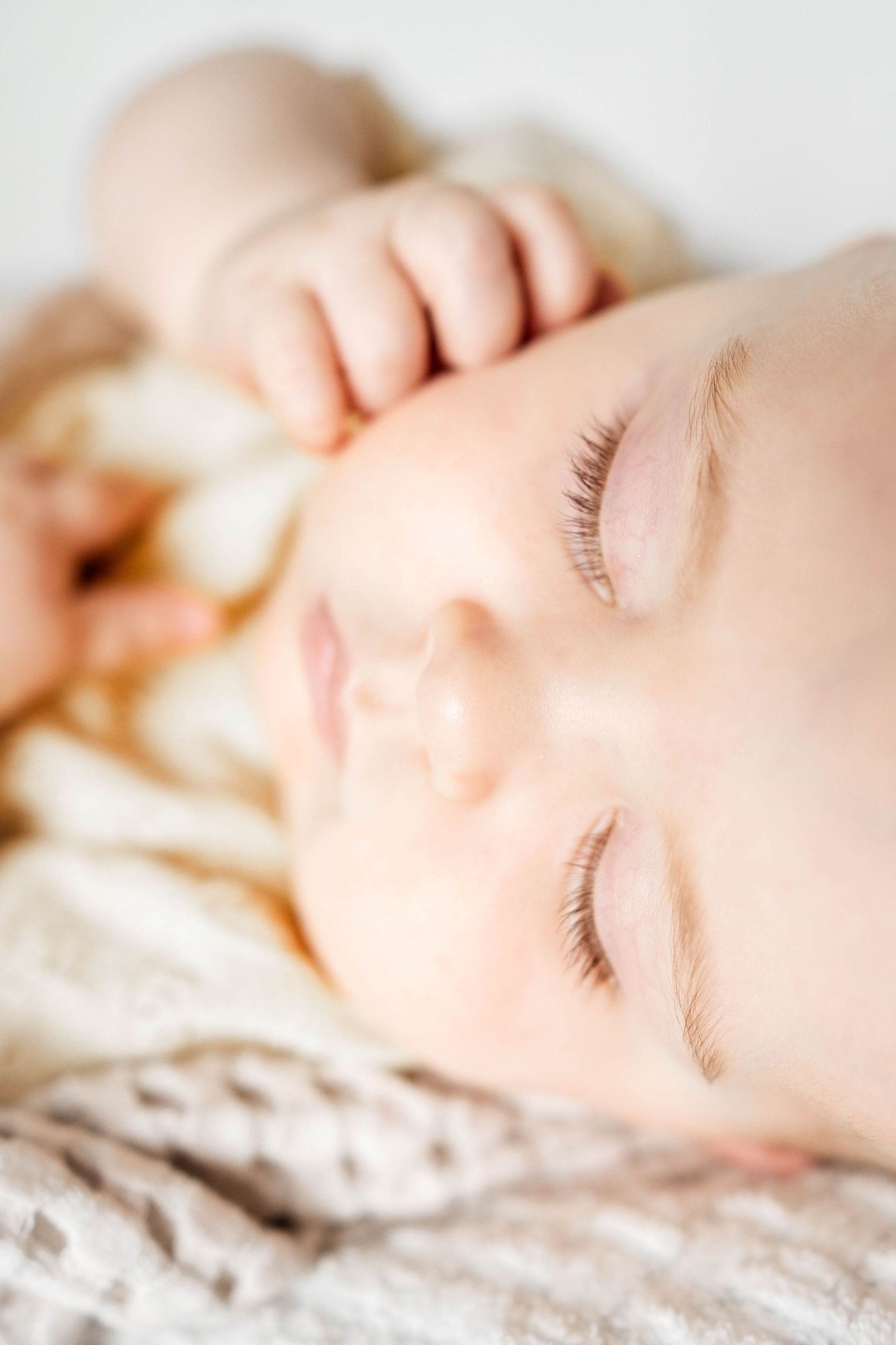 A peaceful sleeping baby with delicate eyelashes resting on a soft cream blanket.