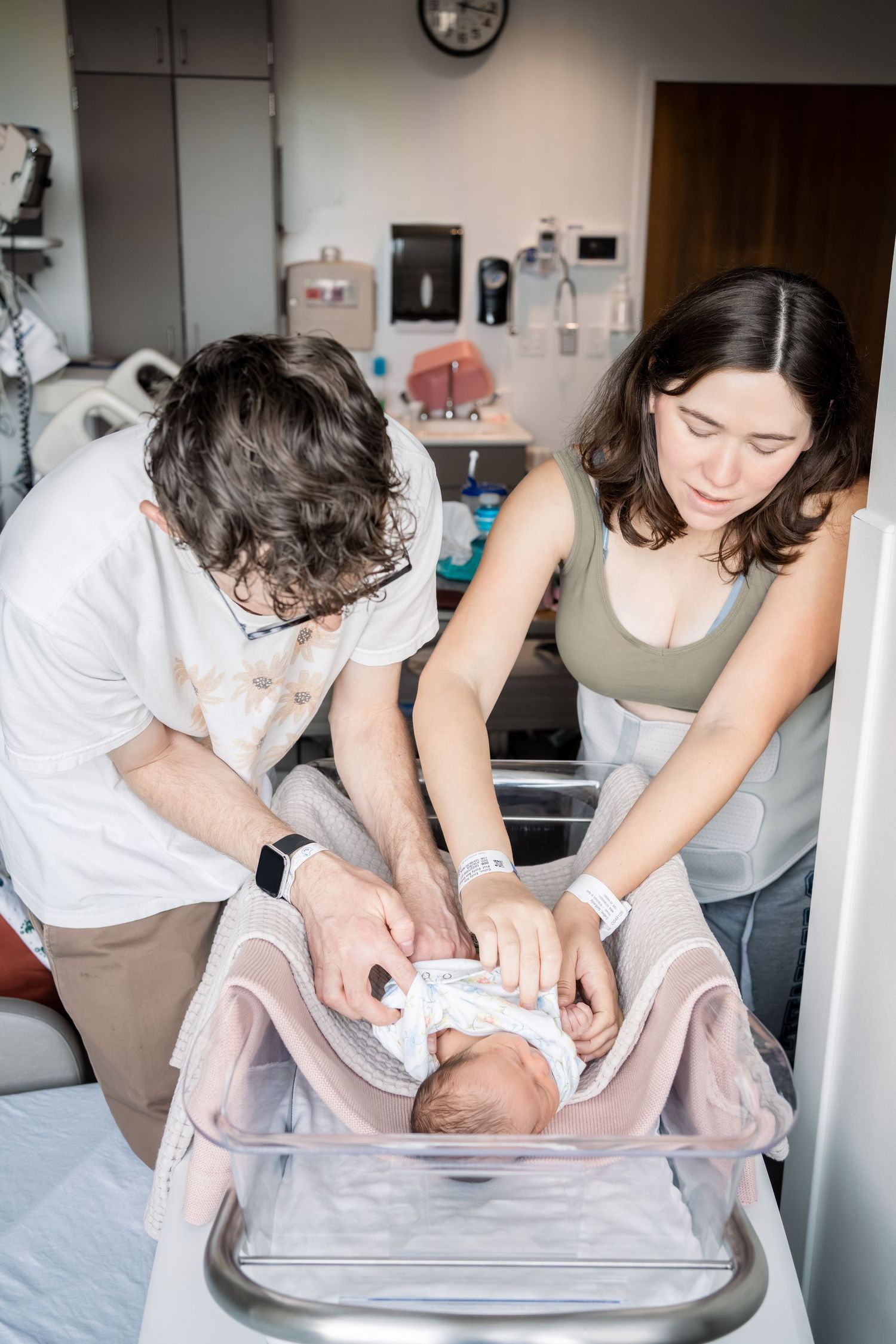 New parents tenderly care for their newborn baby in a hospital bassinet shortly after birth.