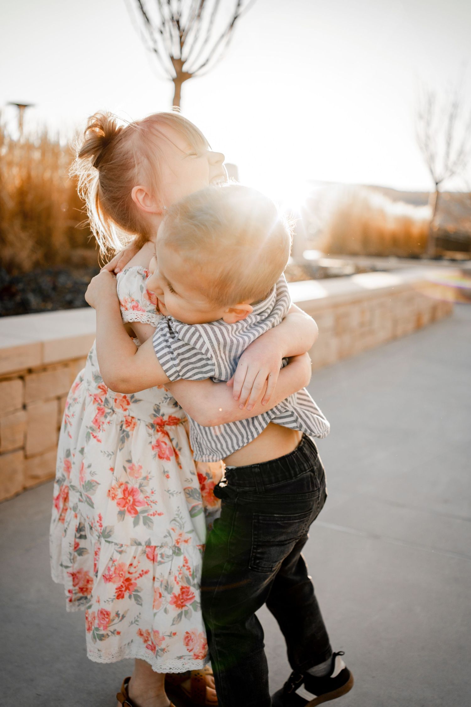 Two young children in casual attire share a sweet embrace while playing together at sunset.