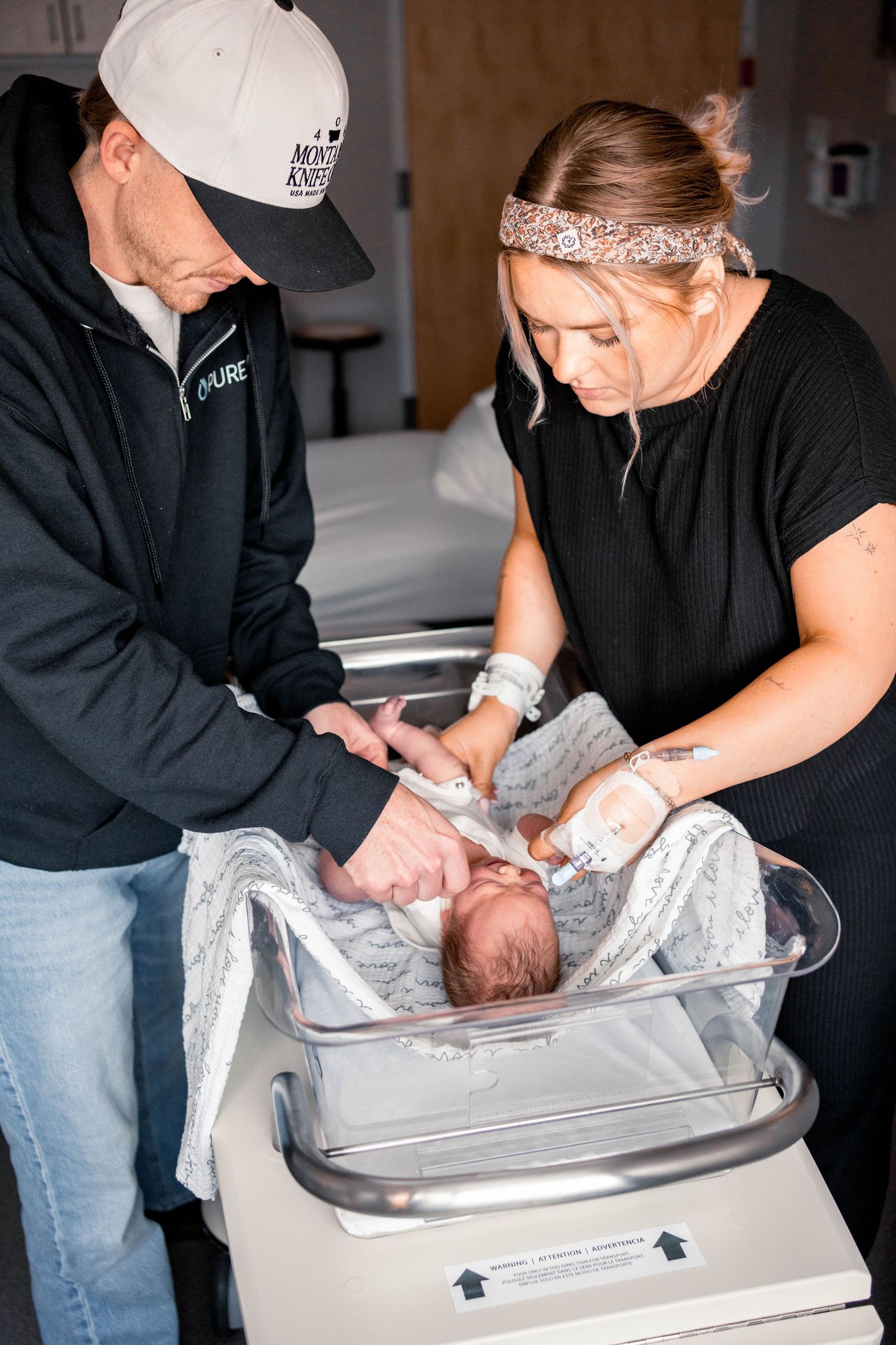 New parents lovingly tend to their swaddled newborn in a hospital bassinet after delivery.