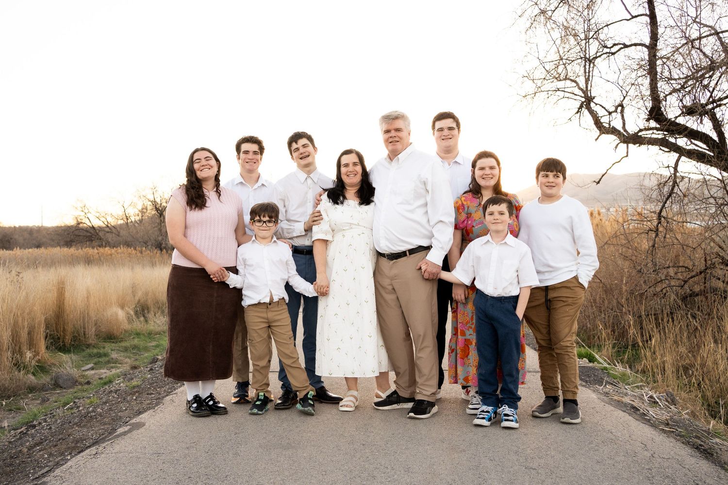A group of people in coordinated white and brown outfits pose together outdoors during a sunset photo session.