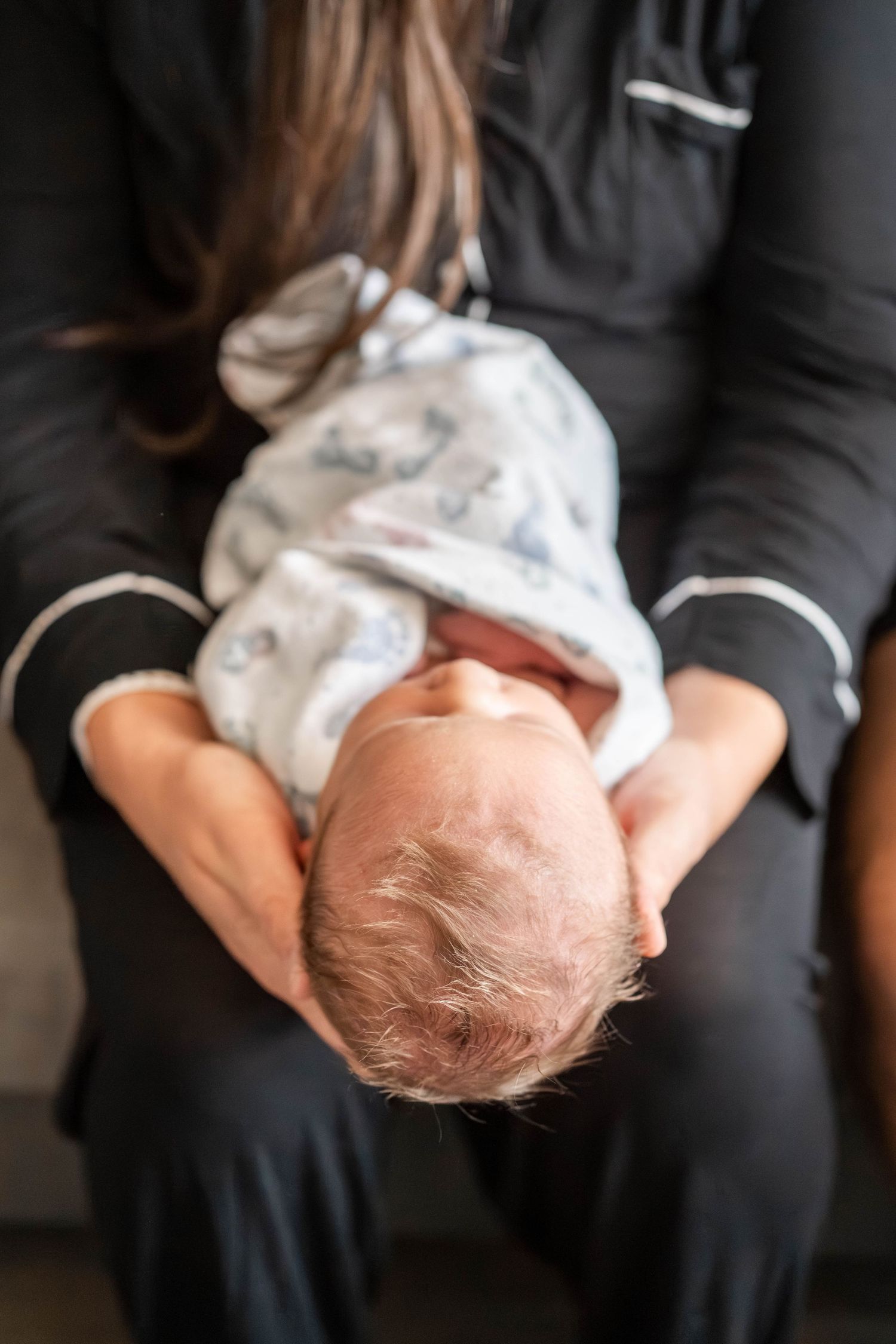 A newborn baby swaddled in a white blanket being cradled in the arms of a person wearing black pajamas.