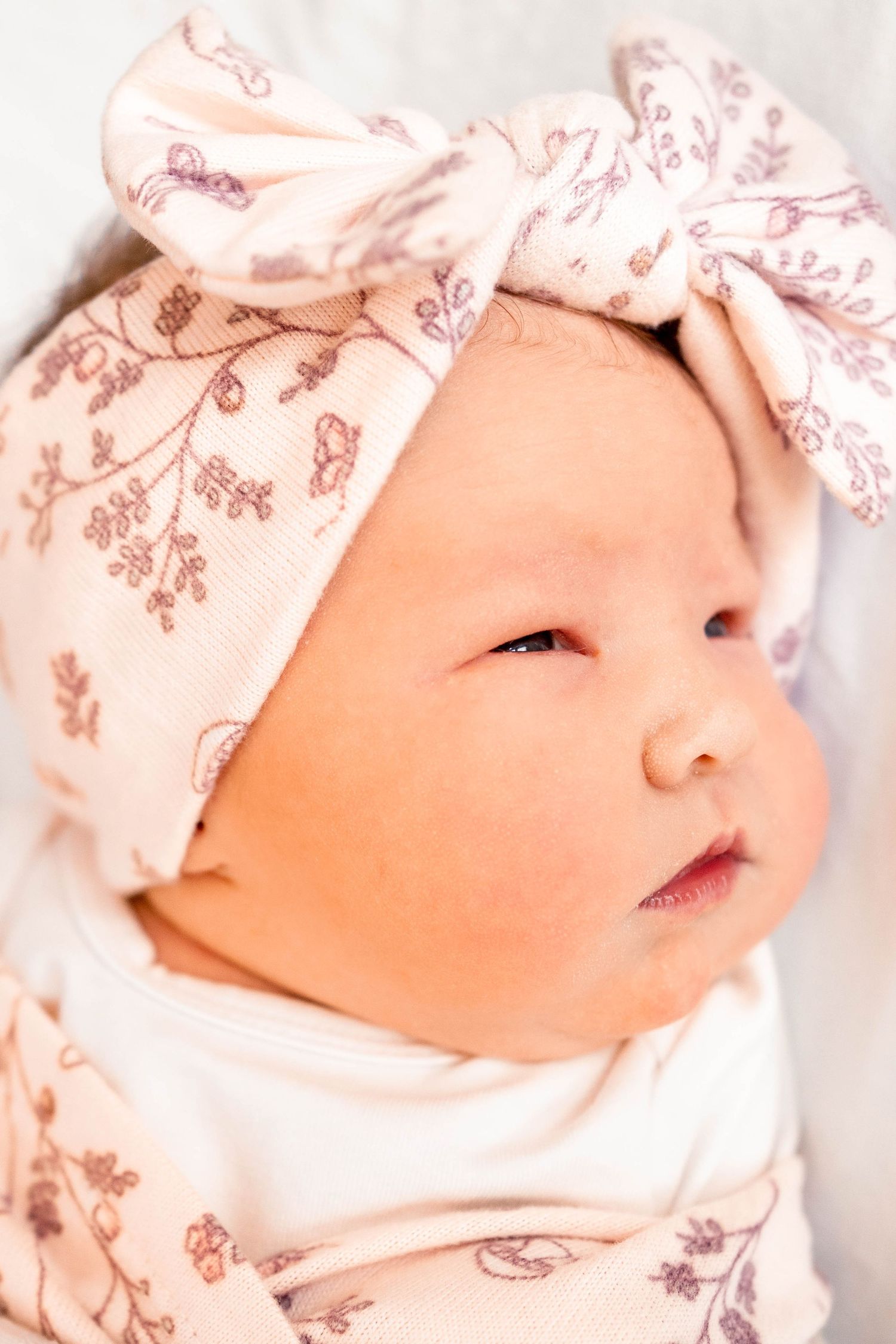 Newborn baby girl wearing a pink floral bow headband, close-up portrait shot.