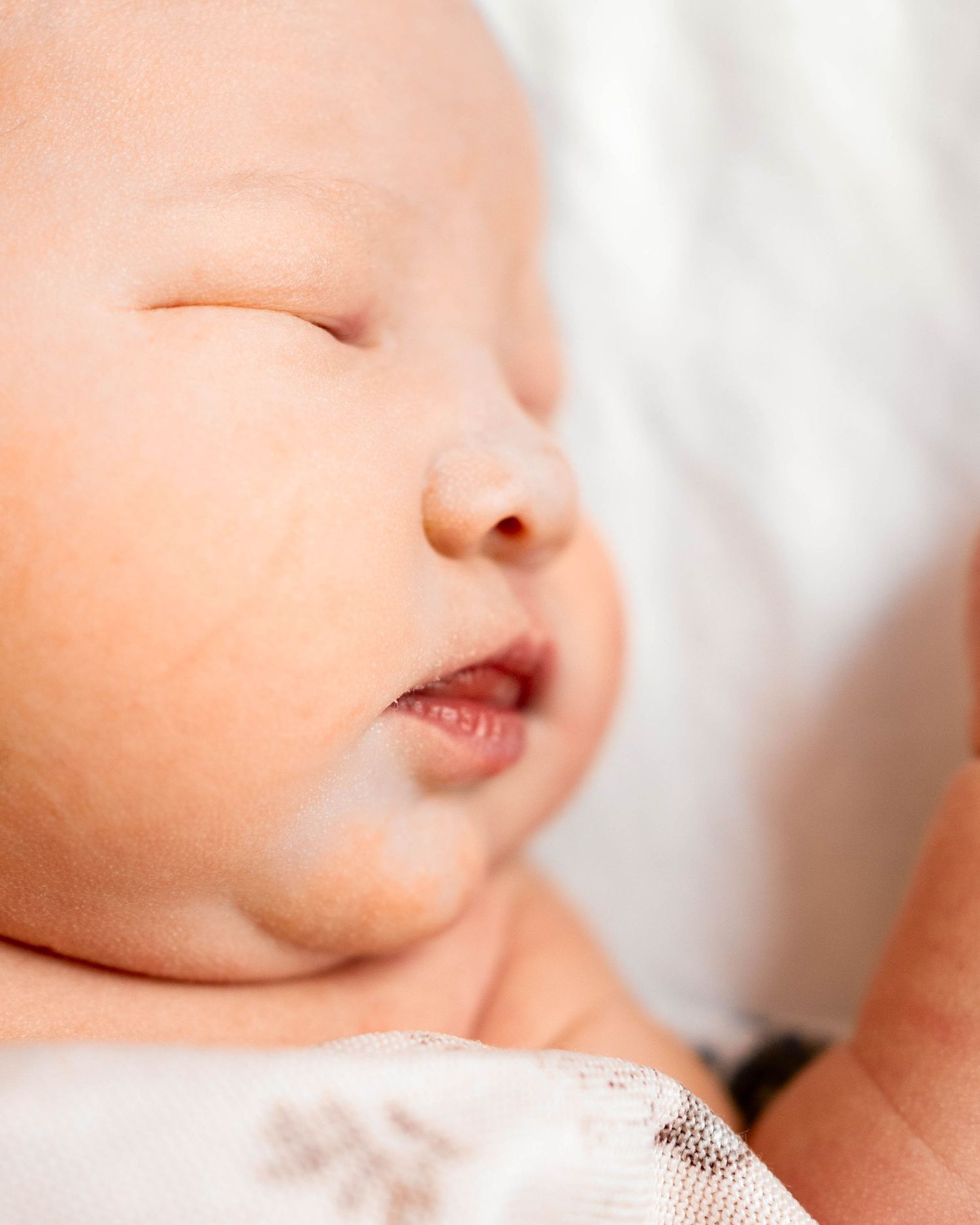 Close-up of a peaceful sleeping newborn baby with soft skin and delicate features resting on a white blanket.