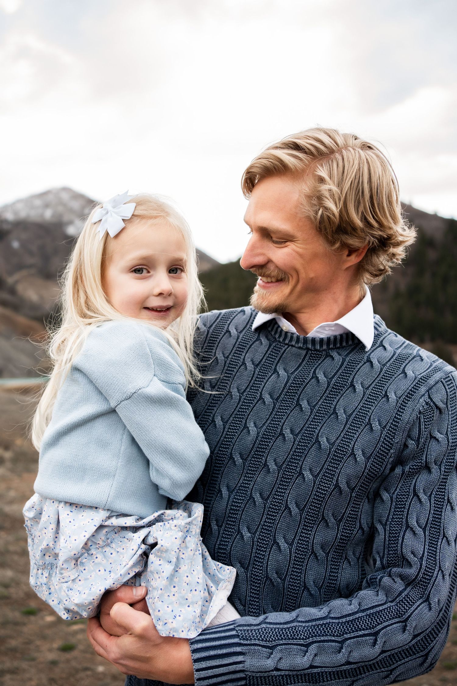 A heartwarming outdoor portrait shows a parent and child sharing a joyful moment against a mountain backdrop.