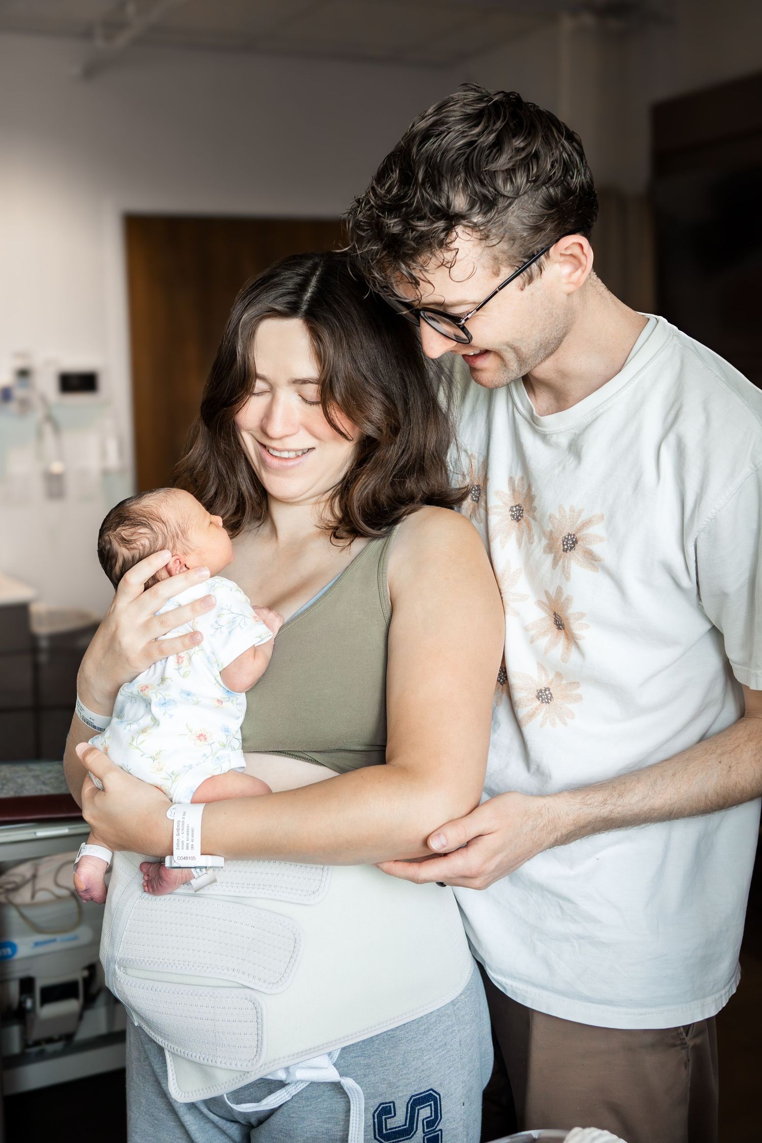 Happy new parents smiling and holding their newborn baby in a hospital room after delivery.