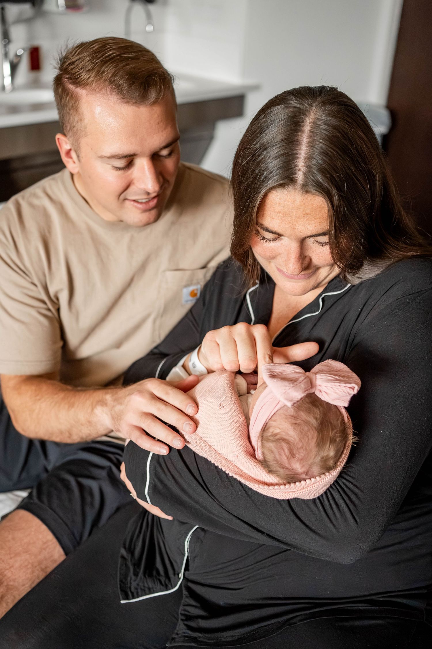Happy parents smiling at their newborn baby wrapped in pink, sharing a tender moment together at home.