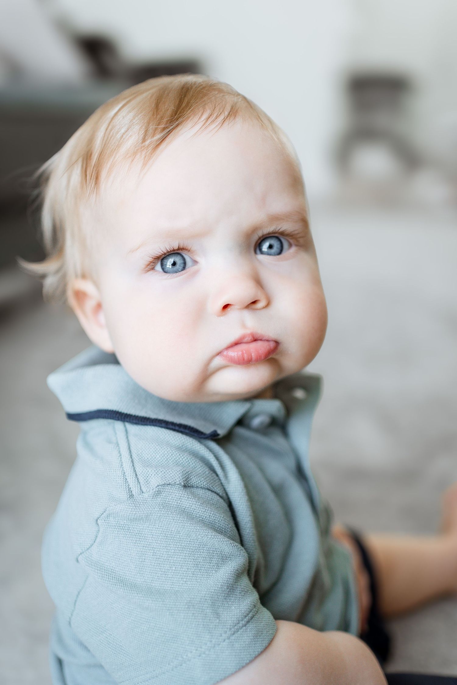 A series of close-up portraits showing a baby with bright blue eyes wearing a gray hoodie making playful expressions.