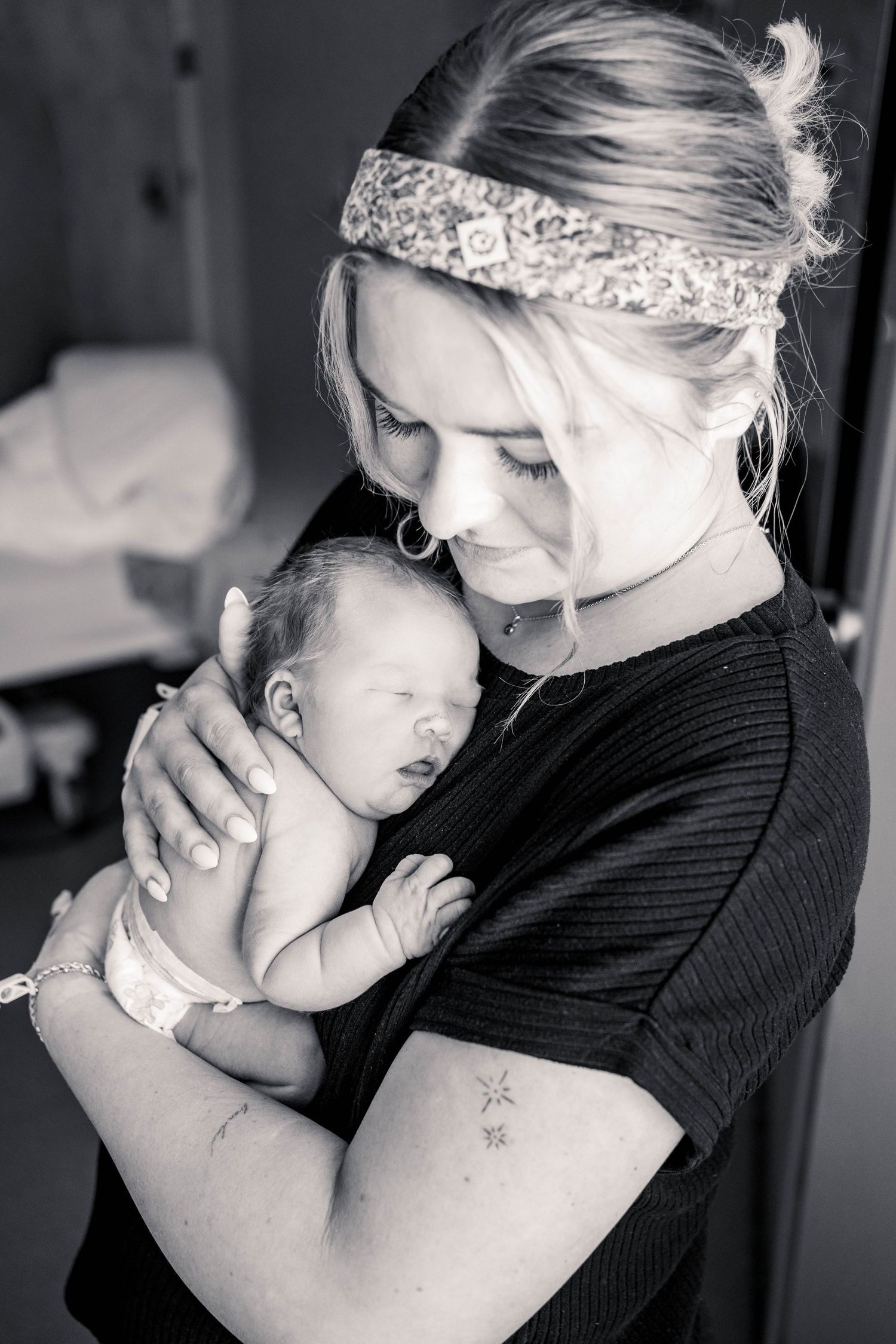 Black and white photo of a young mother tenderly cradling her sleeping newborn baby close to her chest.