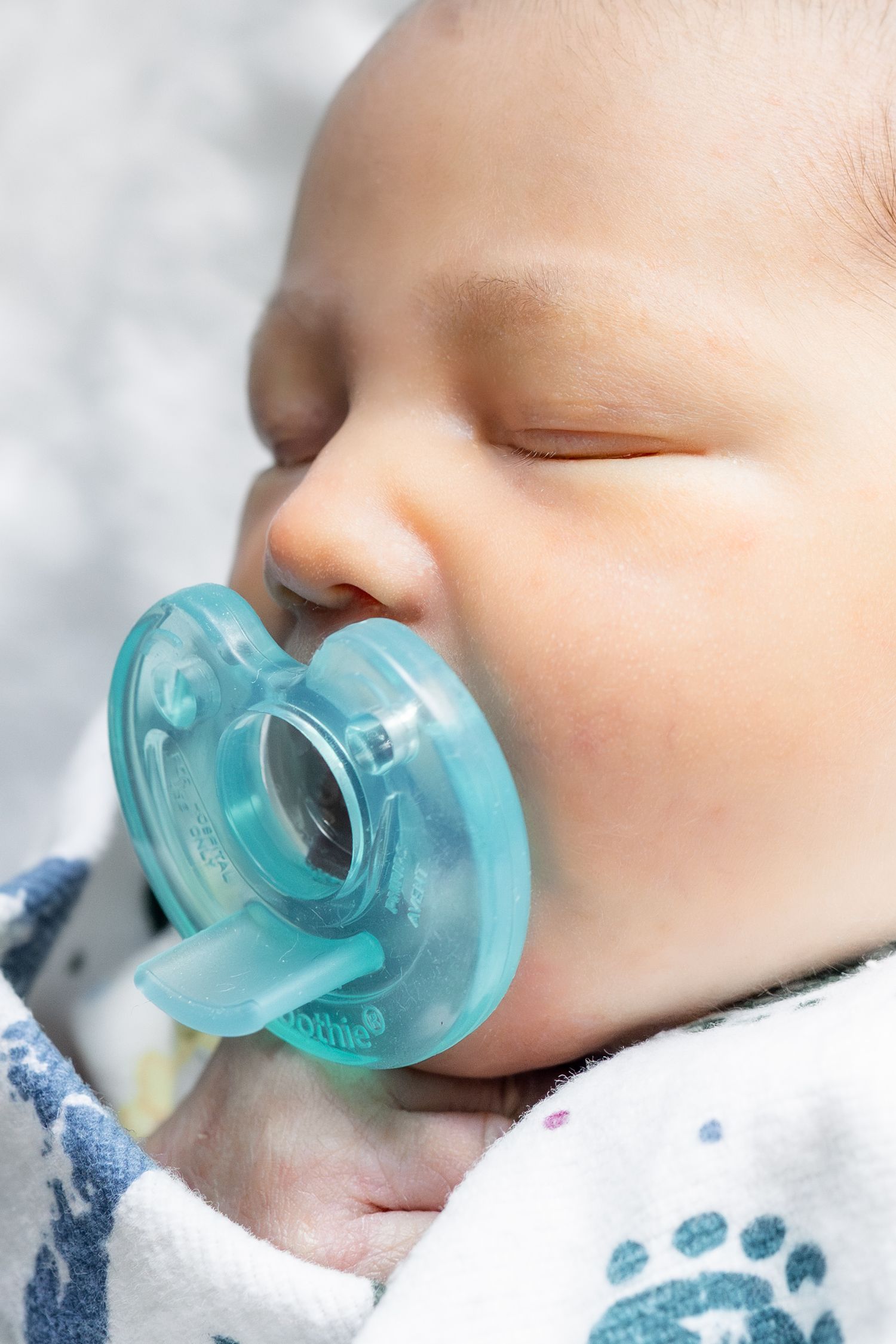 Sleeping newborn baby with a blue pacifier, peacefully resting wrapped in a soft blanket.