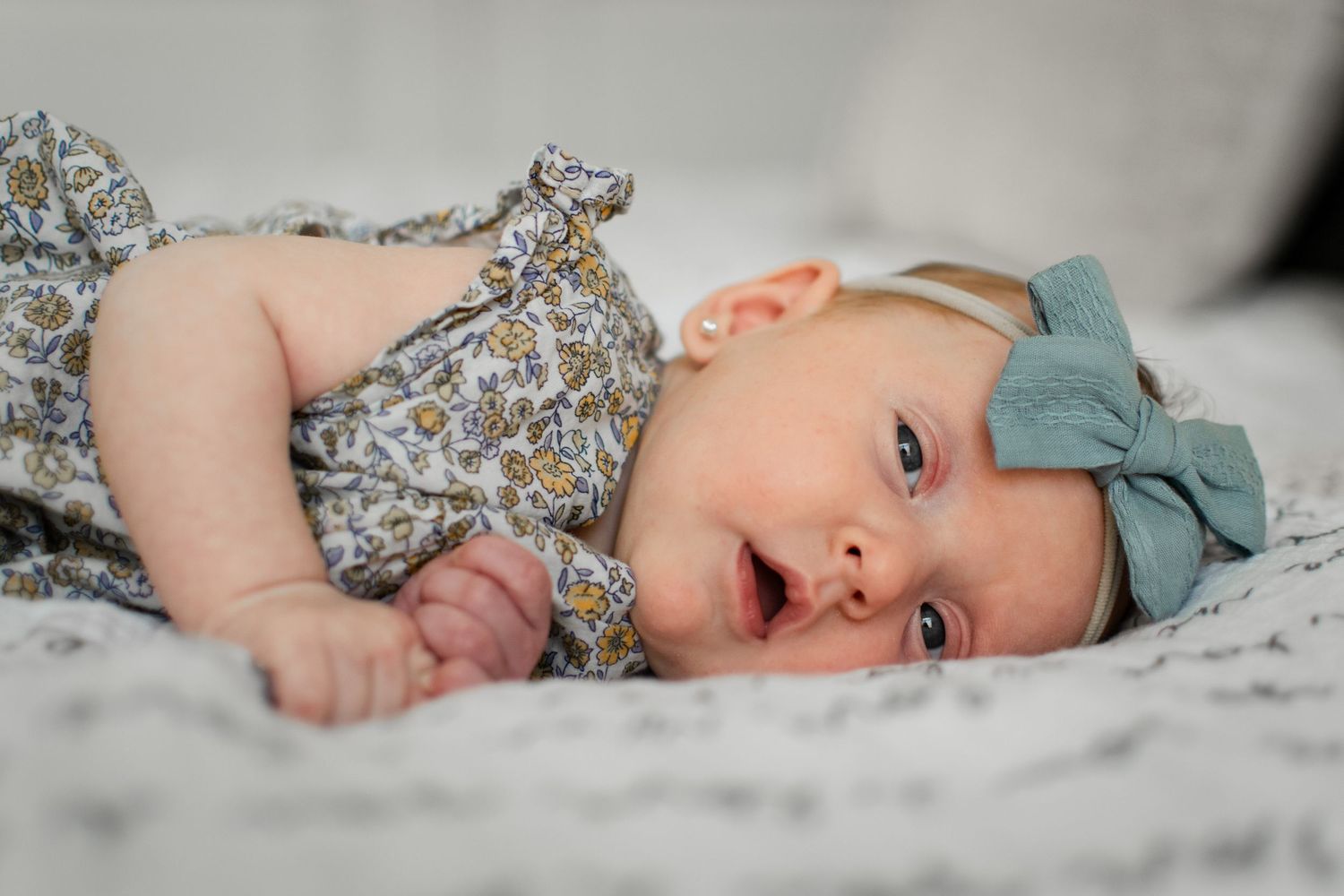 Baby in floral outfit with teal bow resting on textured grey surface.