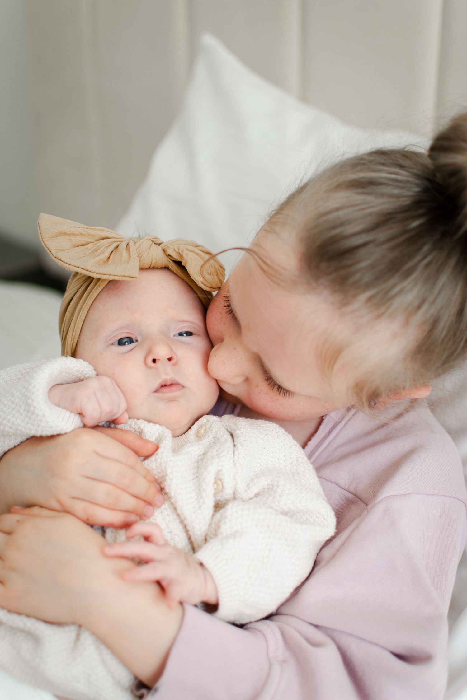 Siblings share tender moment with newborn baby wrapped in white blanket.