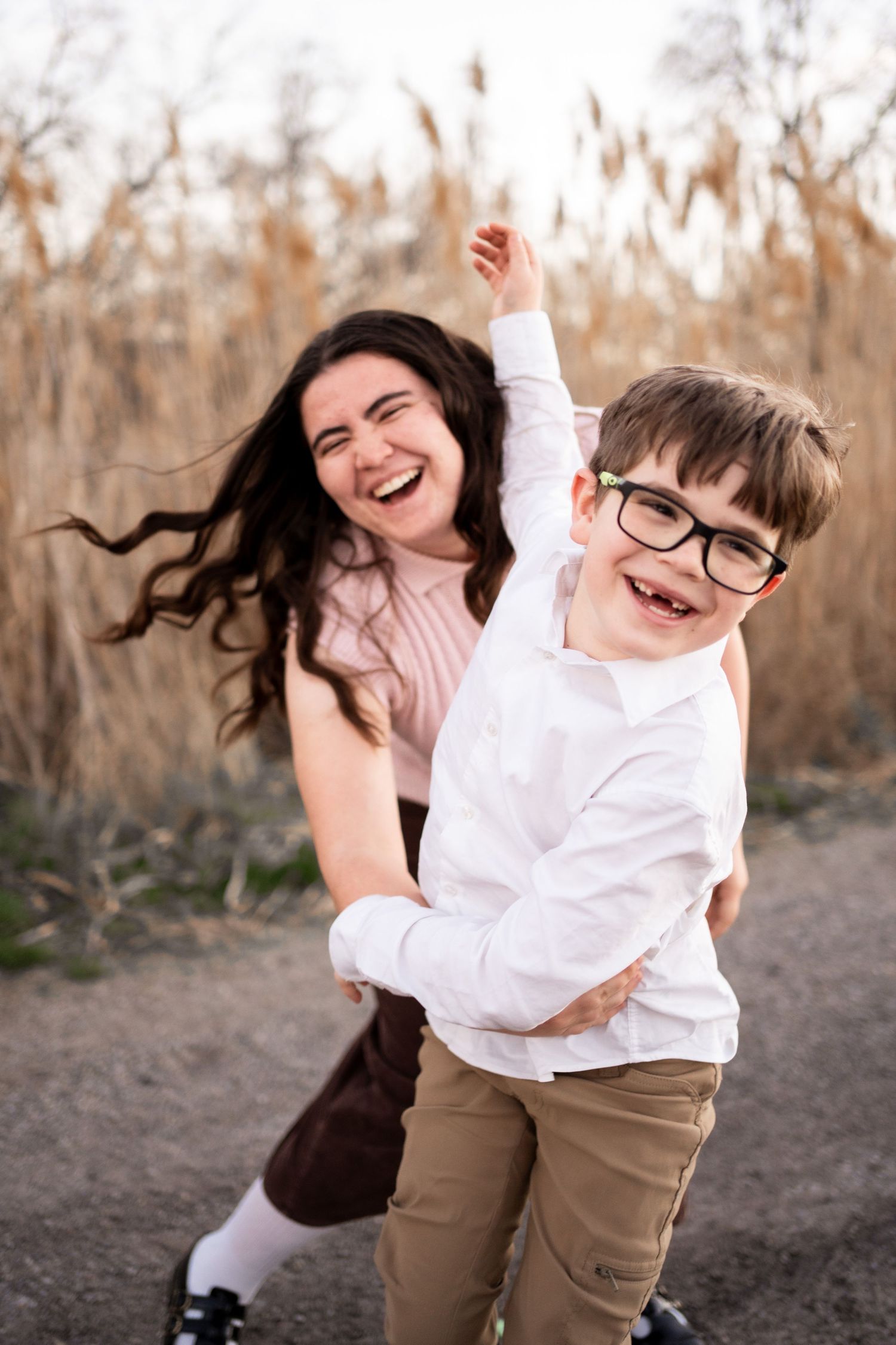 Joyful moment captured outdoors with two people laughing and playing together against a backdrop of autumn reeds.