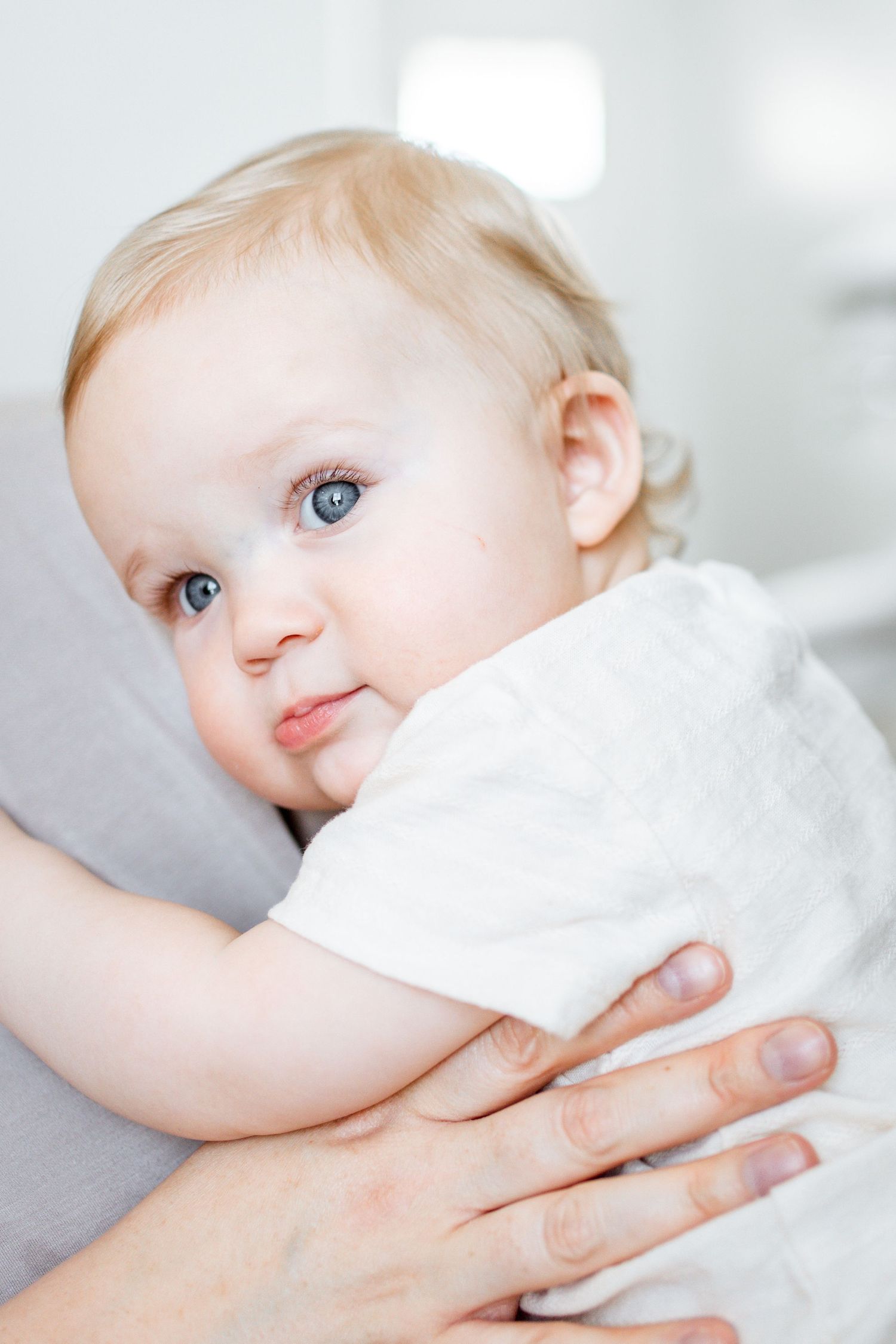 Close-up portrait series of a baby with blue eyes wearing white clothing against a light background.