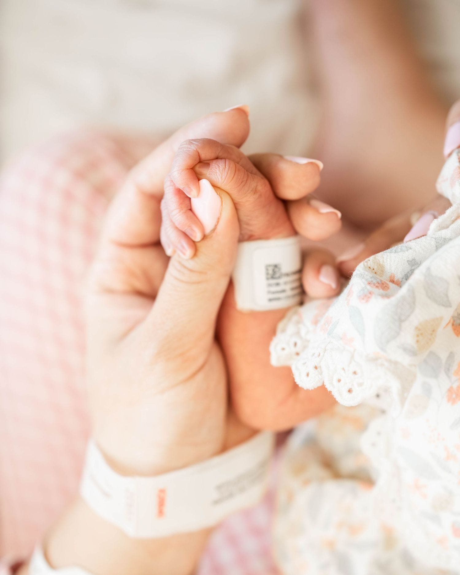 A newborn baby grasping an adult's finger, both wearing hospital ID bracelets, in a tender first moments photo.