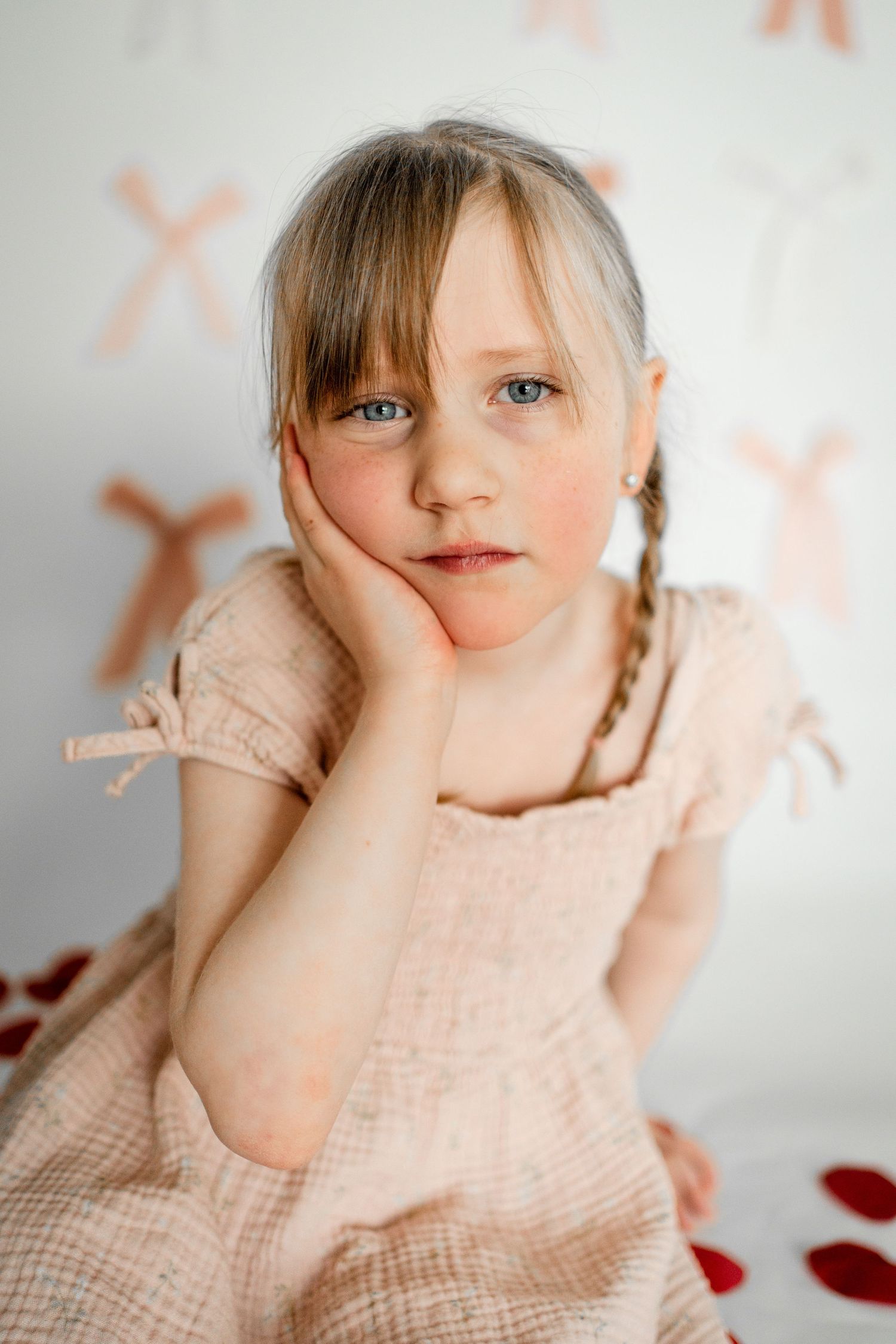 A child in a beige dress poses playfully against a light background with red heart decorations.