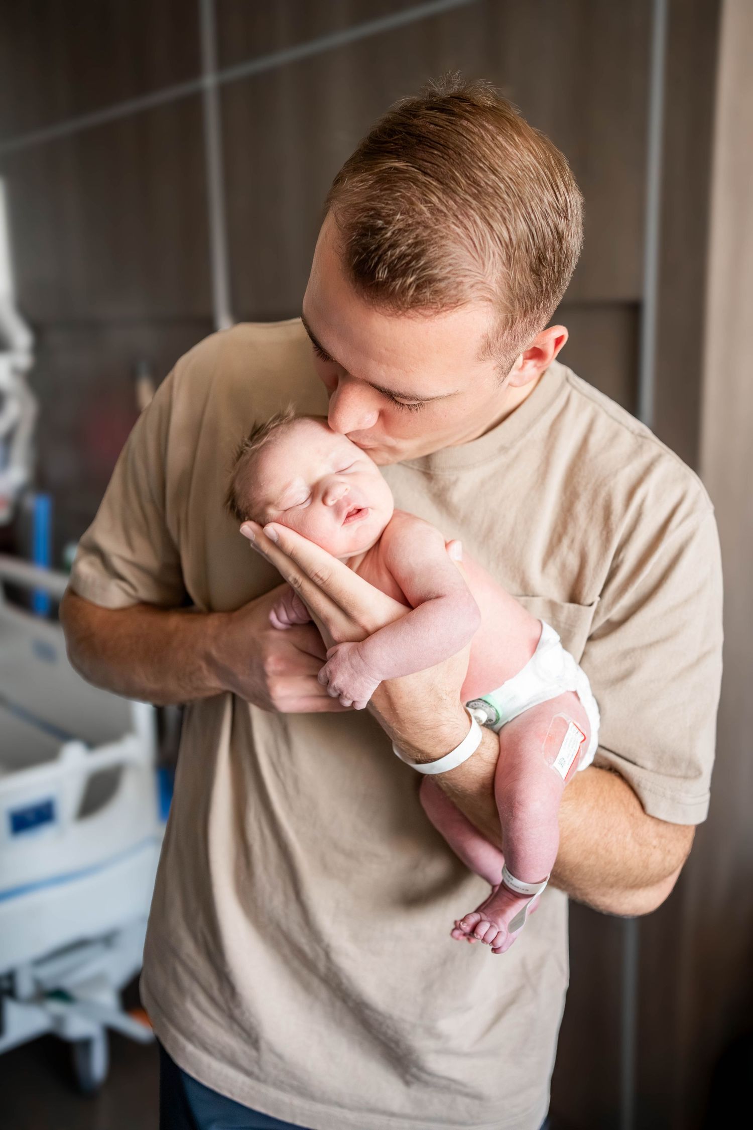 A new father tenderly kisses his sleeping newborn baby while cradling the infant in a hospital room.