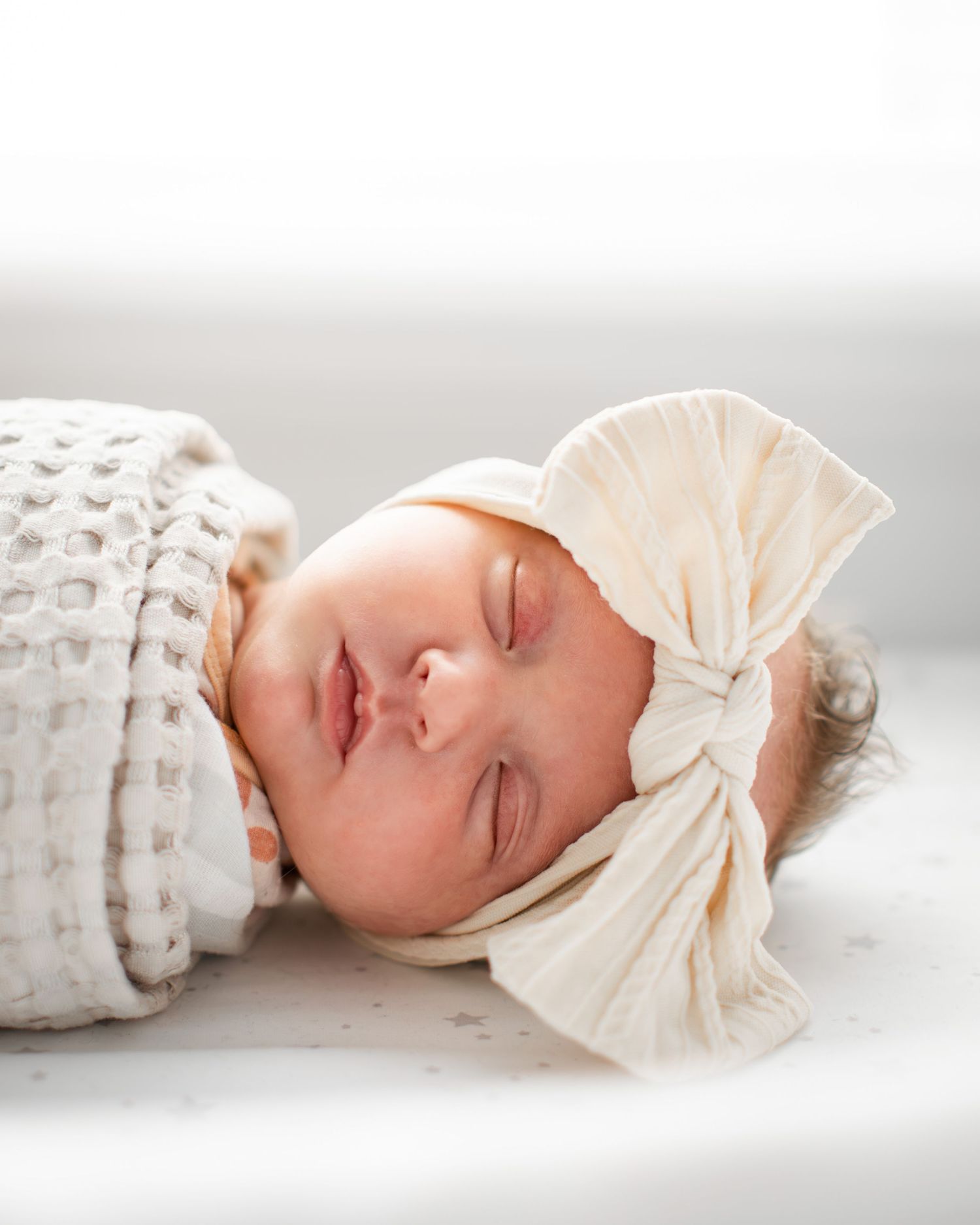Artistic panoramic series of a sleeping newborn baby wrapped in cream fabric lying on a white textured blanket.