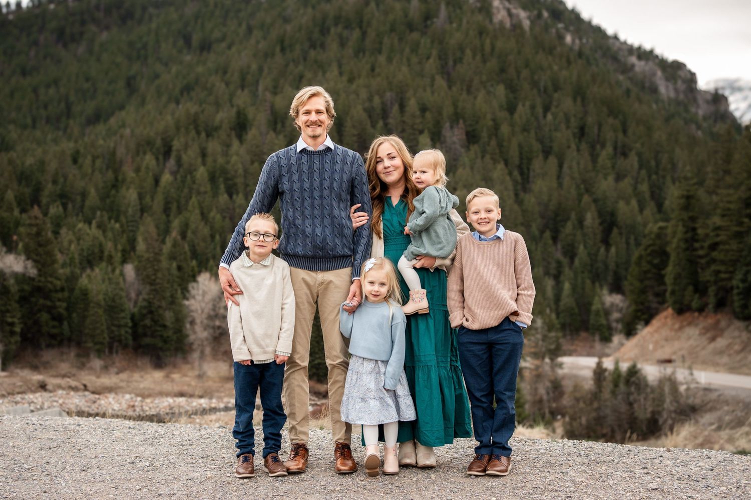 A family enjoying time together on a rocky mountain trail with evergreen trees in the background.