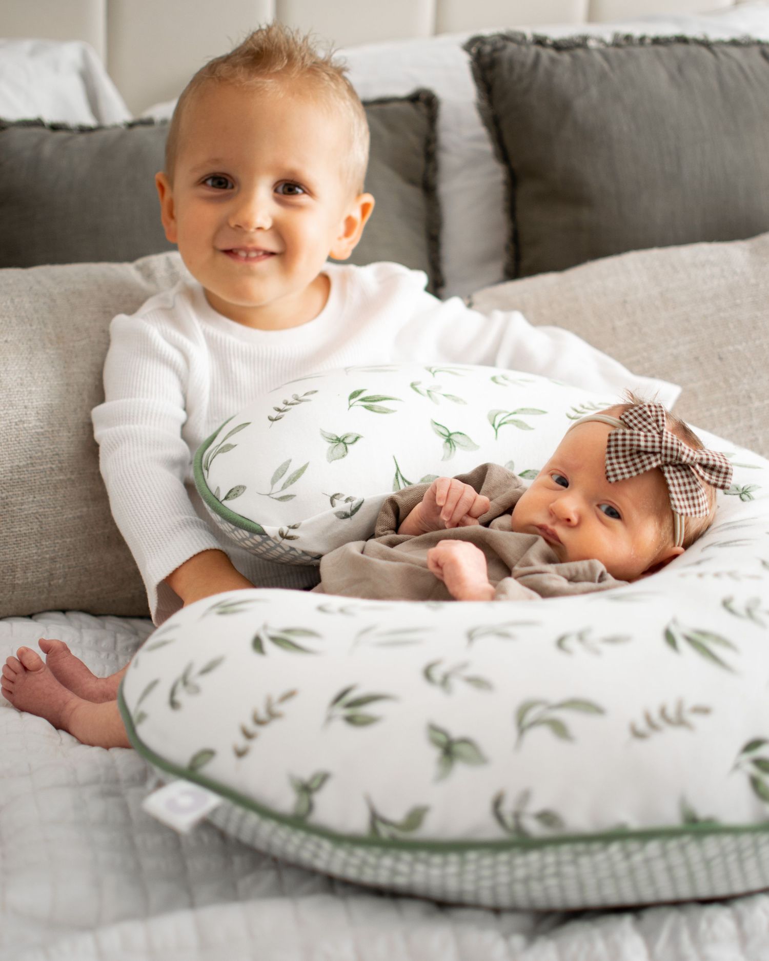 Baby rests on decorative leaf-patterned nursing pillow on grey couch.