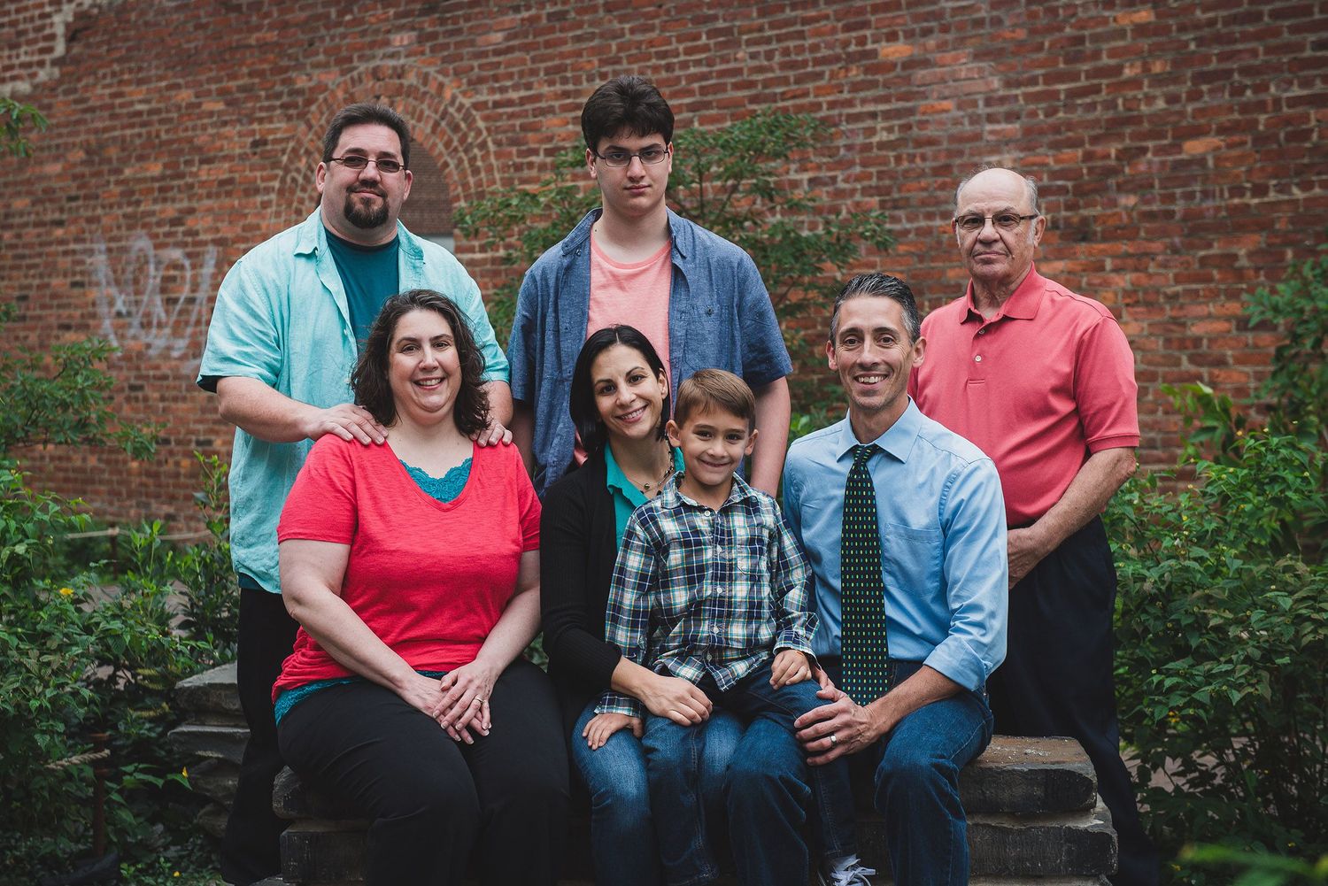 Family group photos against a rustic brick wall backdrop outdoors.