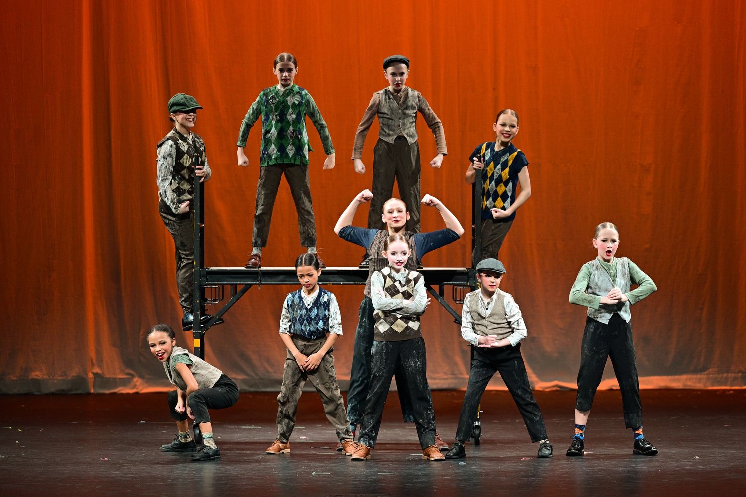 Dancers in traditional German clothing perform a synchronized folk dance routine on a stage with red curtains.