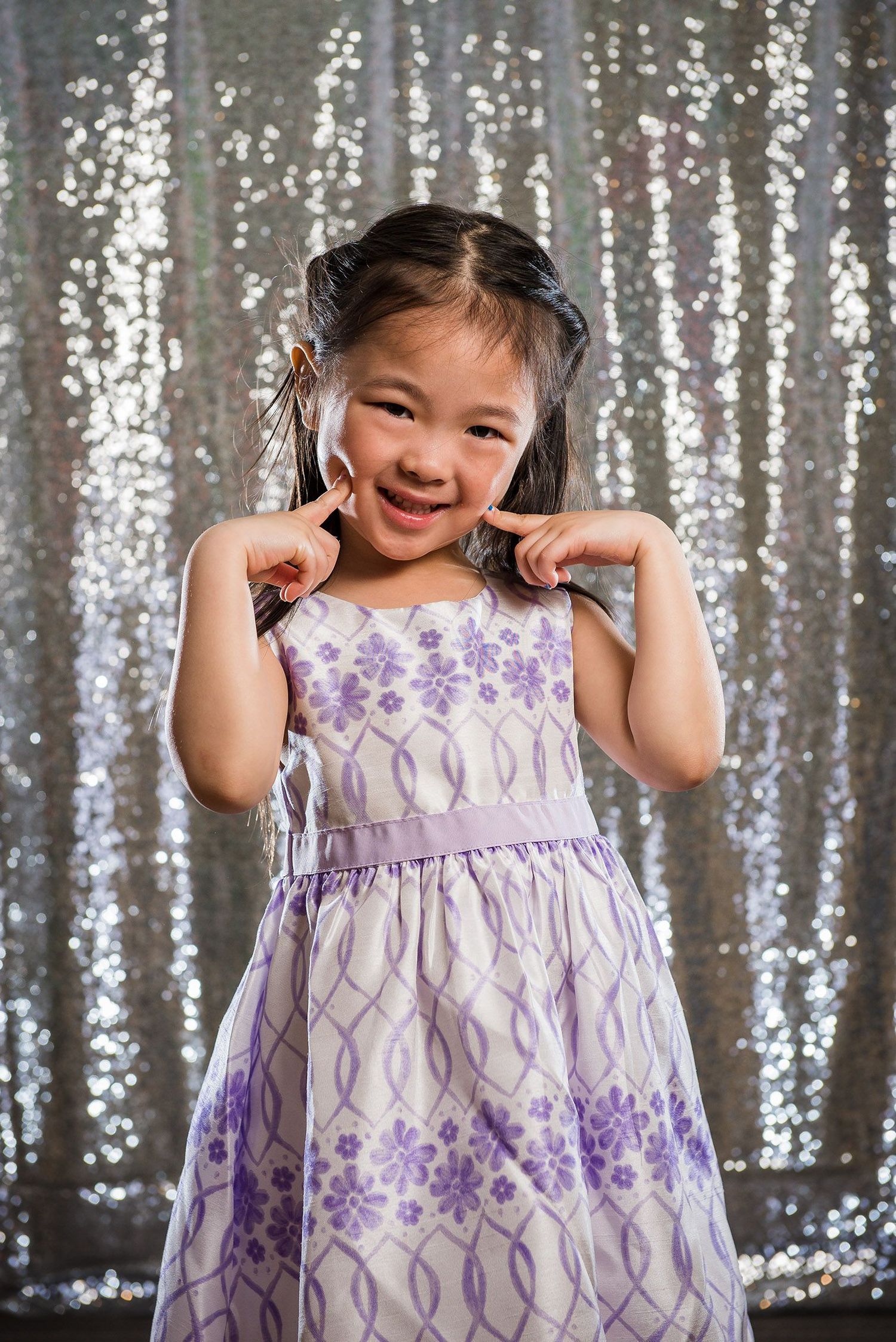 Young dancer in purple and white dress twirling against sparkly silver backdrop.