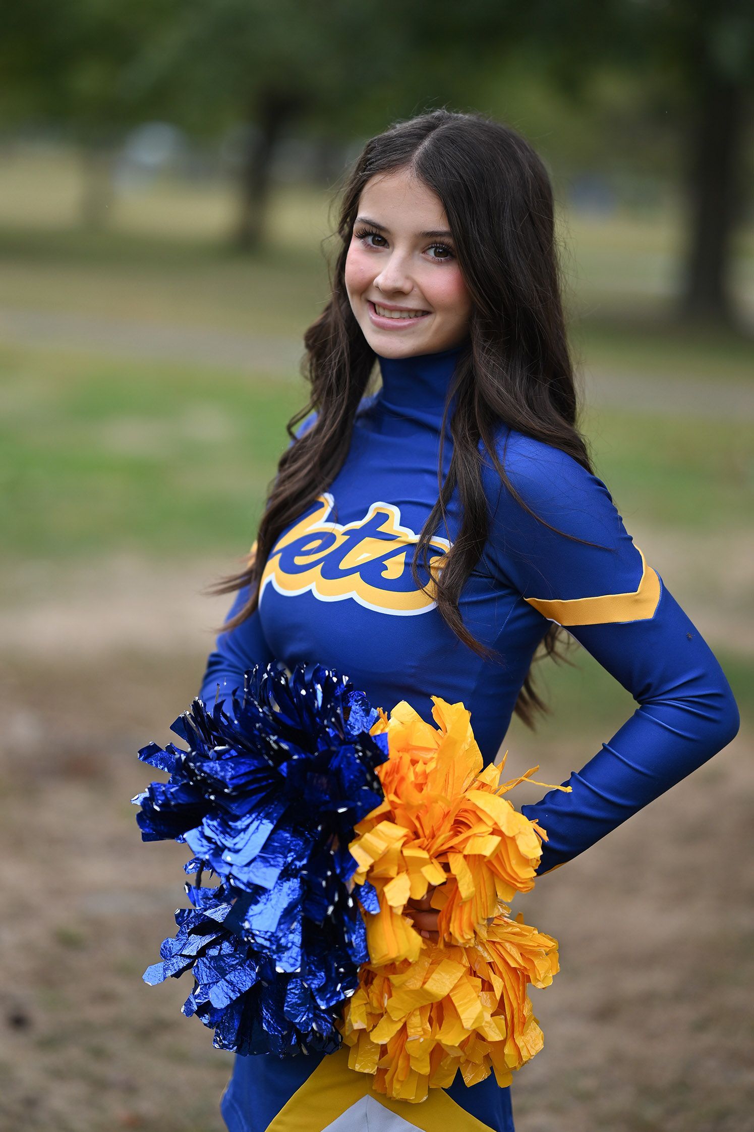 Cheerleader in blue and gold uniform holding pom poms outdoors.