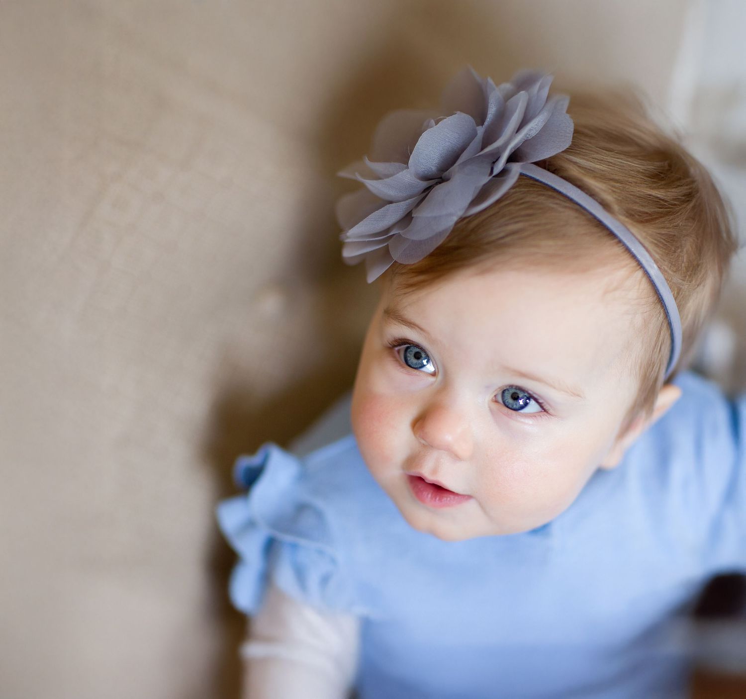 Baby wearing blue outfit with bow accessory looking up at camera.