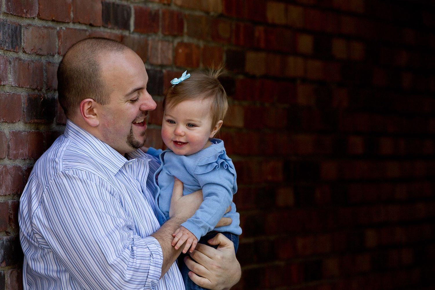 Father and child share playful moments against brick wall background in casual setting.
