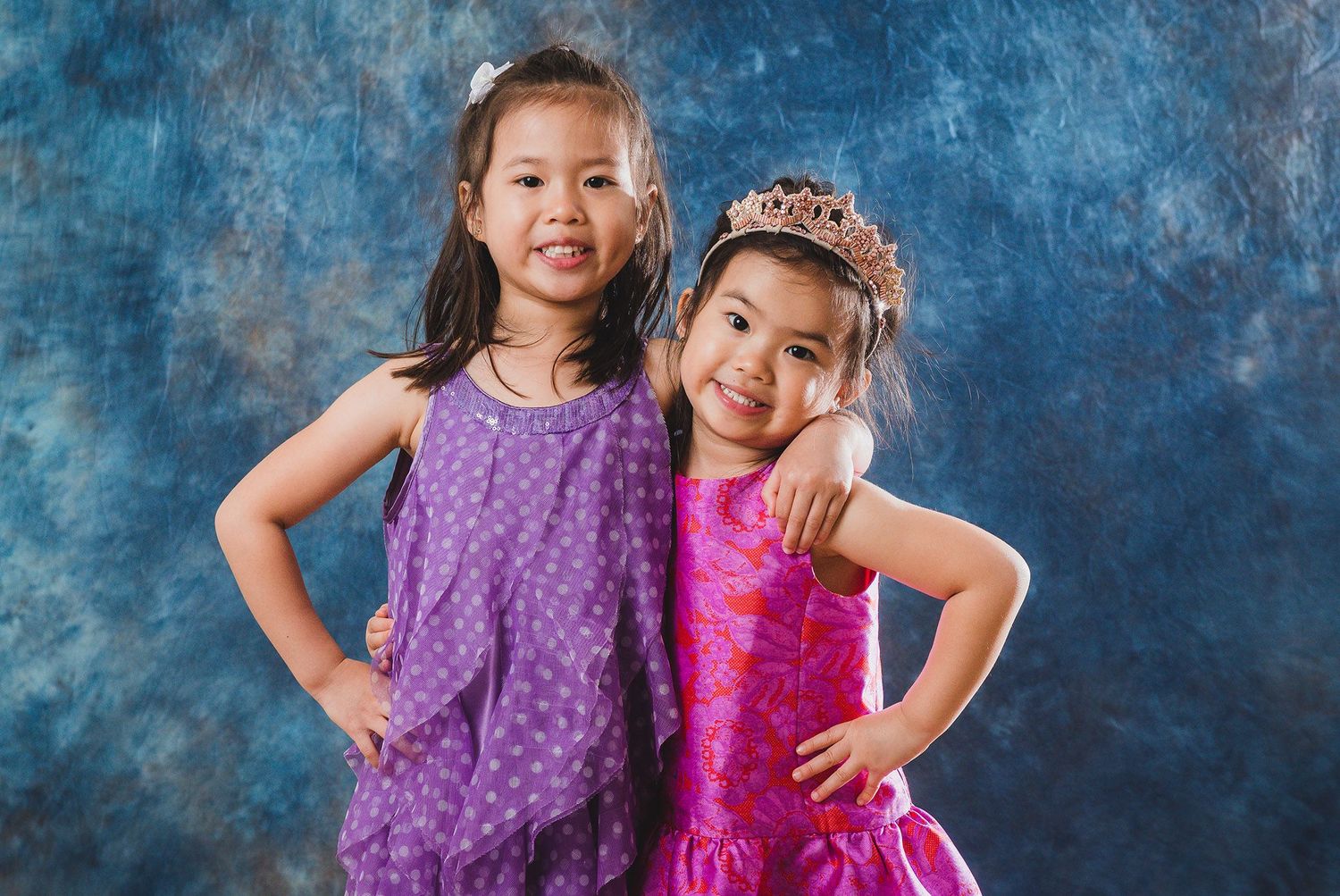Children in purple and pink dresses posing together against blue background.