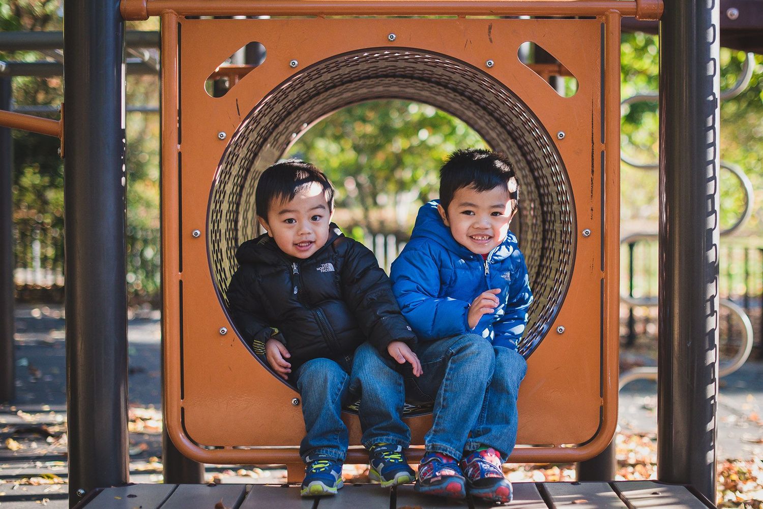 Two children sitting together in circular playground equipment frame.