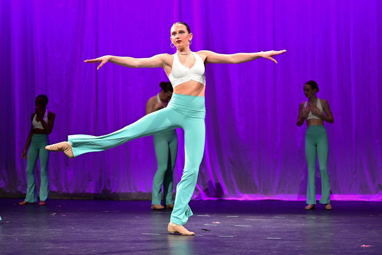 Dancers perform a graceful sequence in colorful costumes against a vibrant purple stage backdrop.