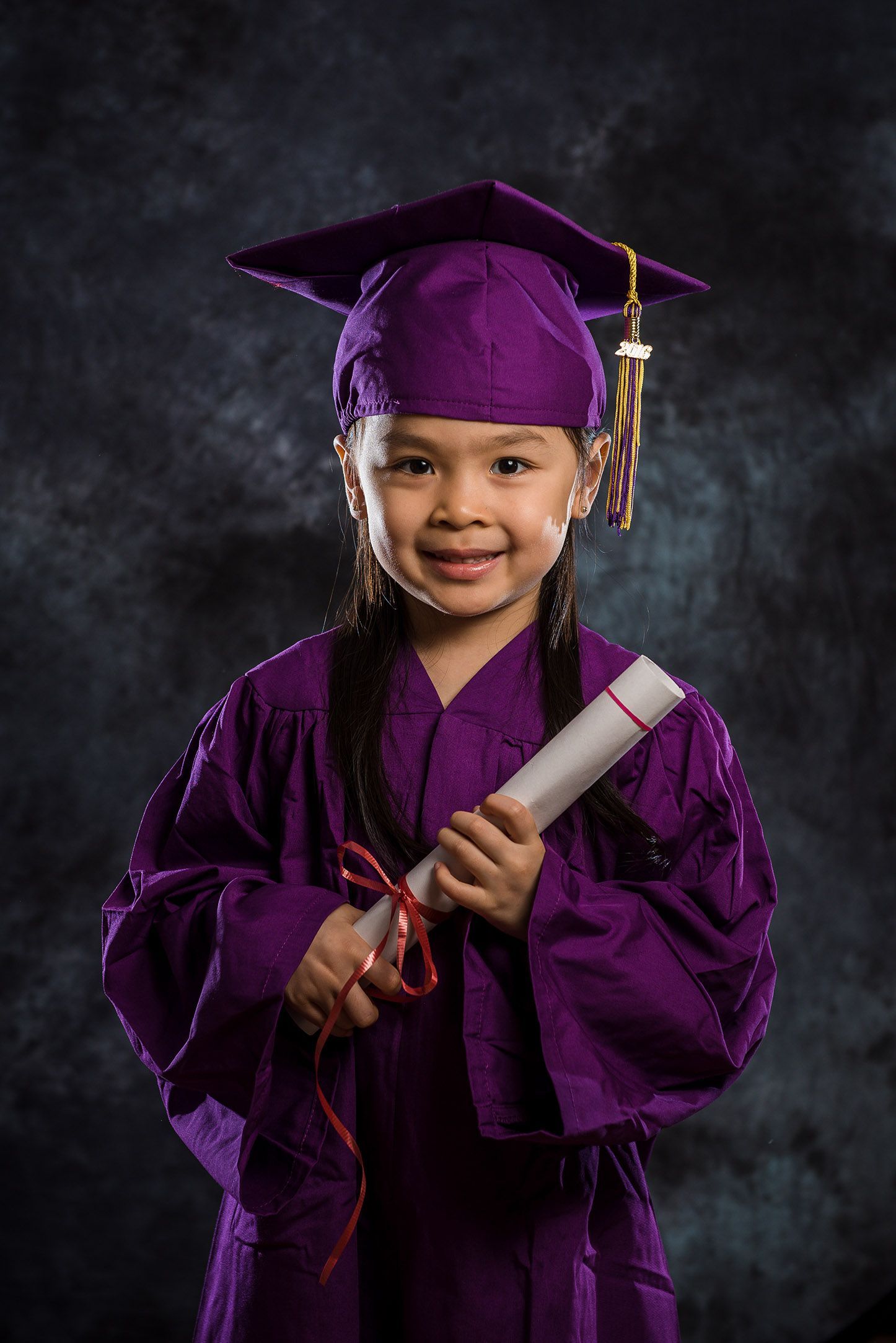 Graduation photos featuring small graduate in purple cap and gown holding diploma.